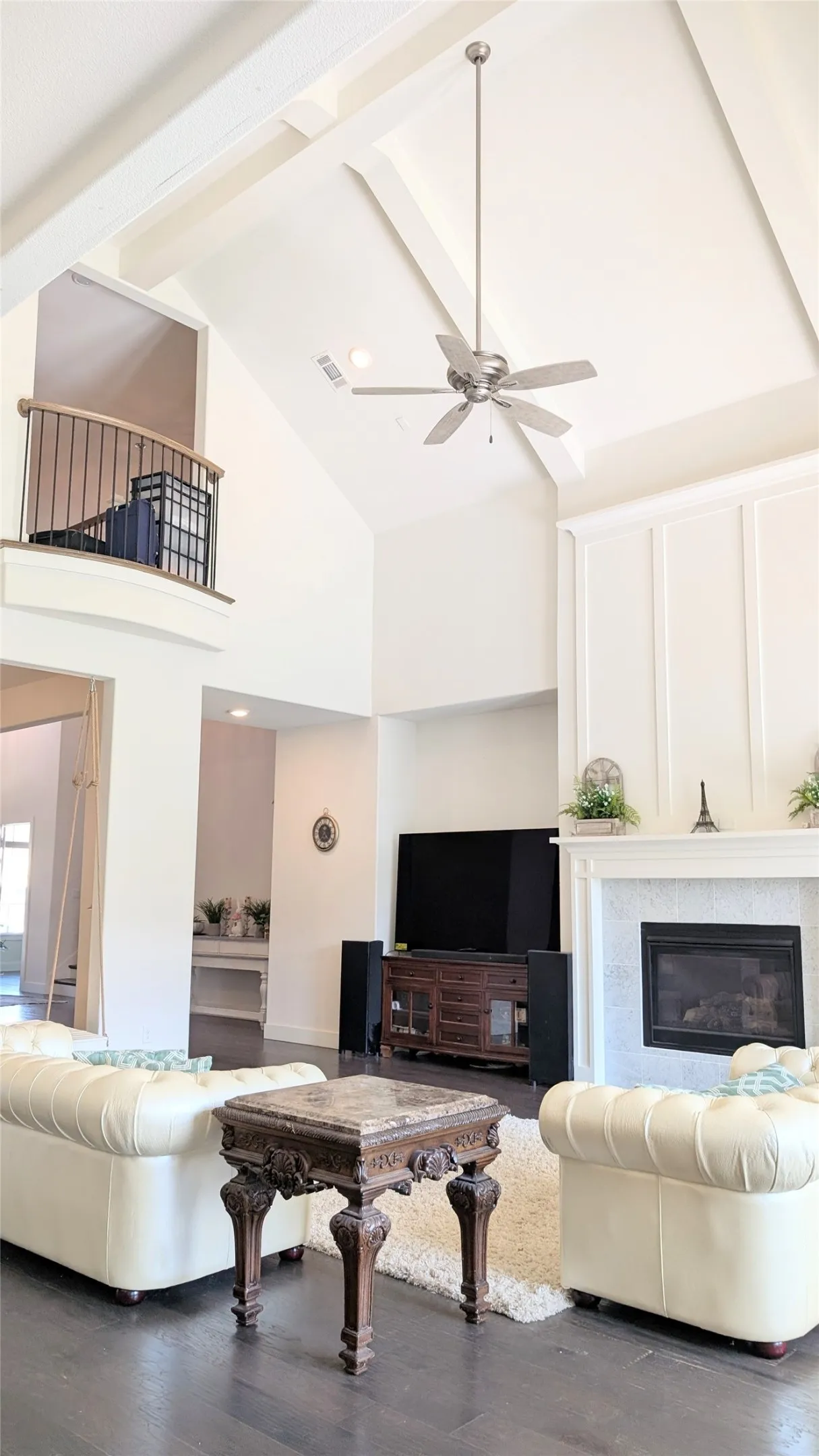 Two-story living area featuring vaulted ceilings with exposed beams, dark wood-finish flooring, and a fireplace with a stone surround and paneled mantel