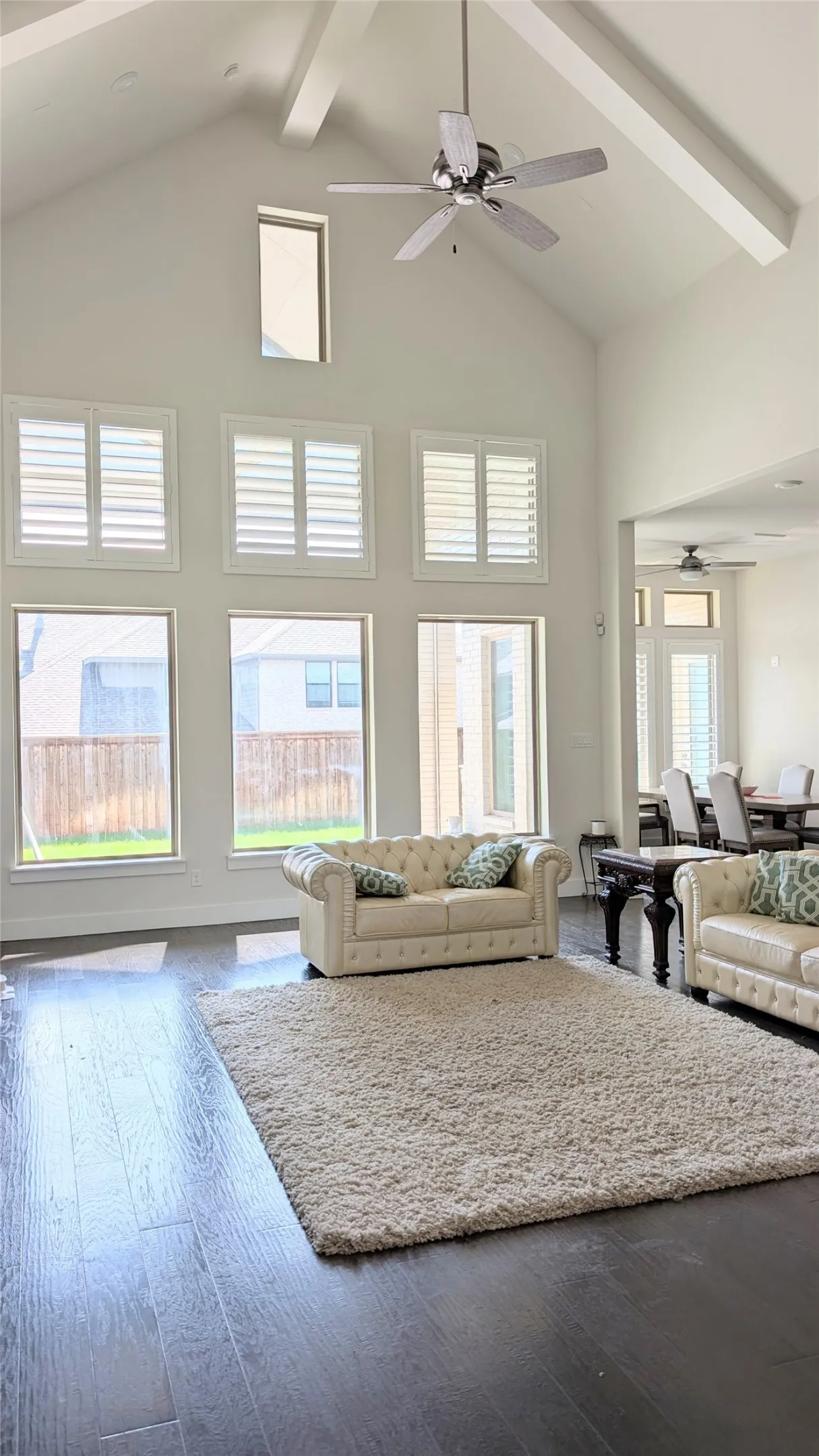 Double-height living area featuring dark wood-finish flooring, a vaulted ceiling with exposed beams, and a ceiling fan