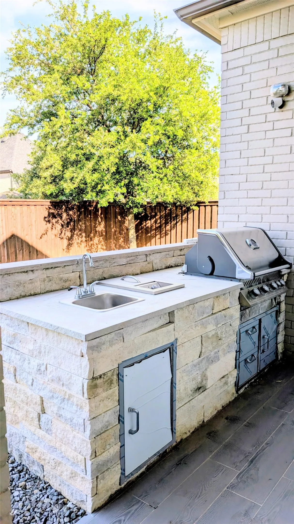 Outdoor kitchen featuring a built-in stainless steel grill, integrated sink, and stone-clad cabinetry, all set on a patio with decorative concrete flooring
