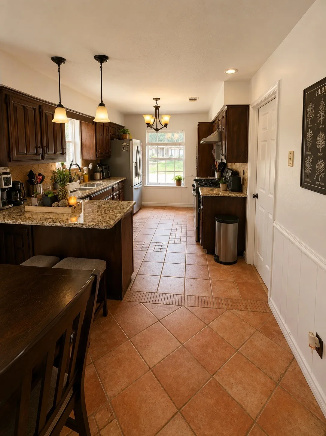 Kitchen featuring wood-finish cabinetry, granite-style countertops, stainless steel appliances, and terra cotta-style tile flooring