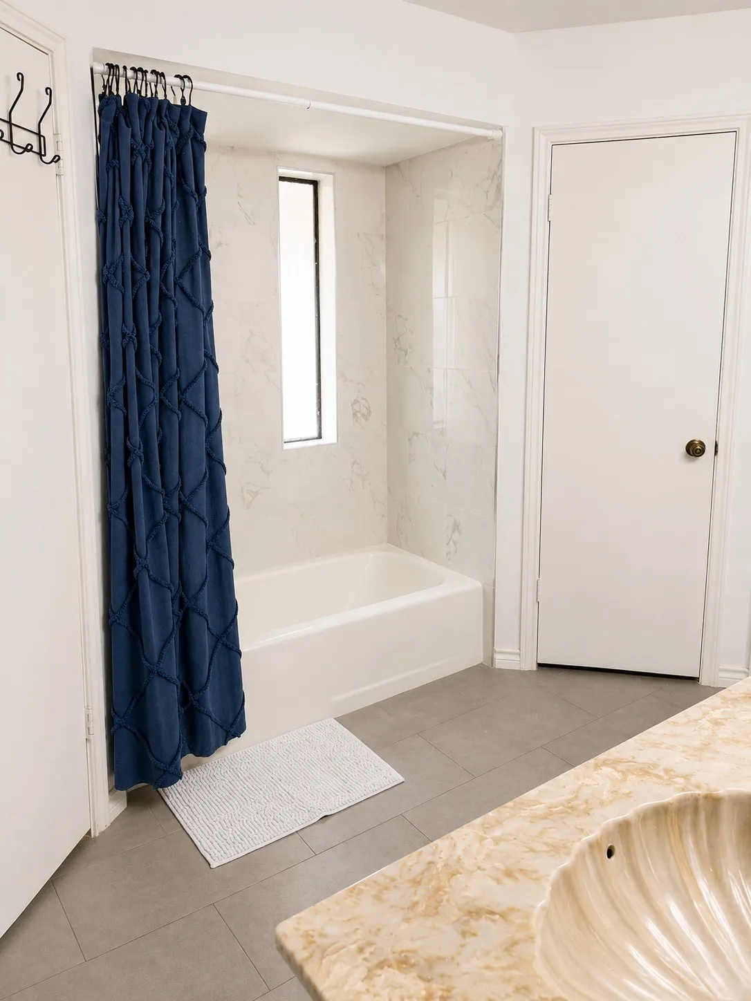 Bathroom featuring a built-in tub with a vertical window, tiled surround, and stone-finish vanity with an integrated shell-motif​​‌​​​​‌​​‌‌​‌‌​​​‌‌​‌​‌​‌​​​‌​​ sink