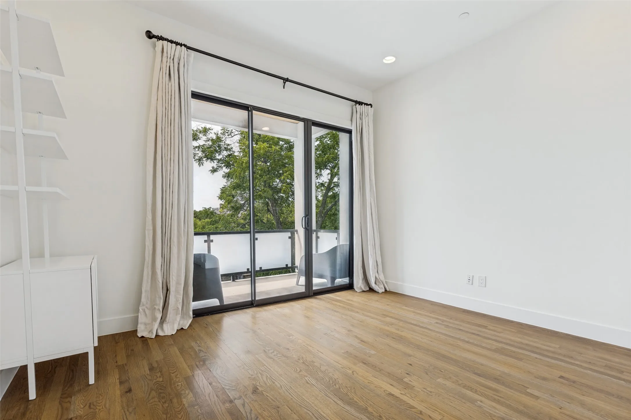 Hardwood flooring throughout this room featuring a sliding glass door to a private balcony with a glass railing