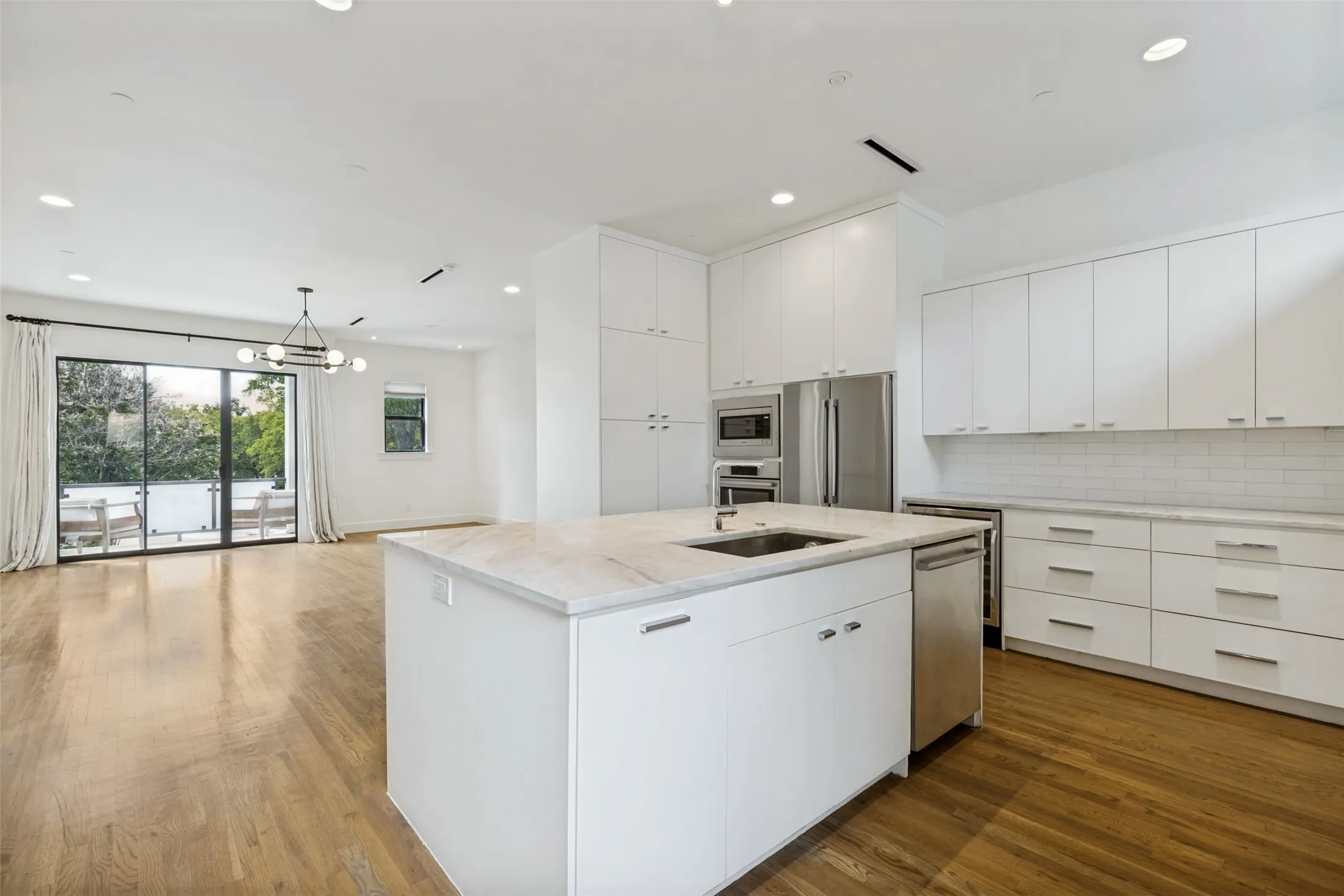 Contemporary kitchen featuring a large island with an undermount sink, white cabinetry, stainless steel appliances, and wood-finish flooring
