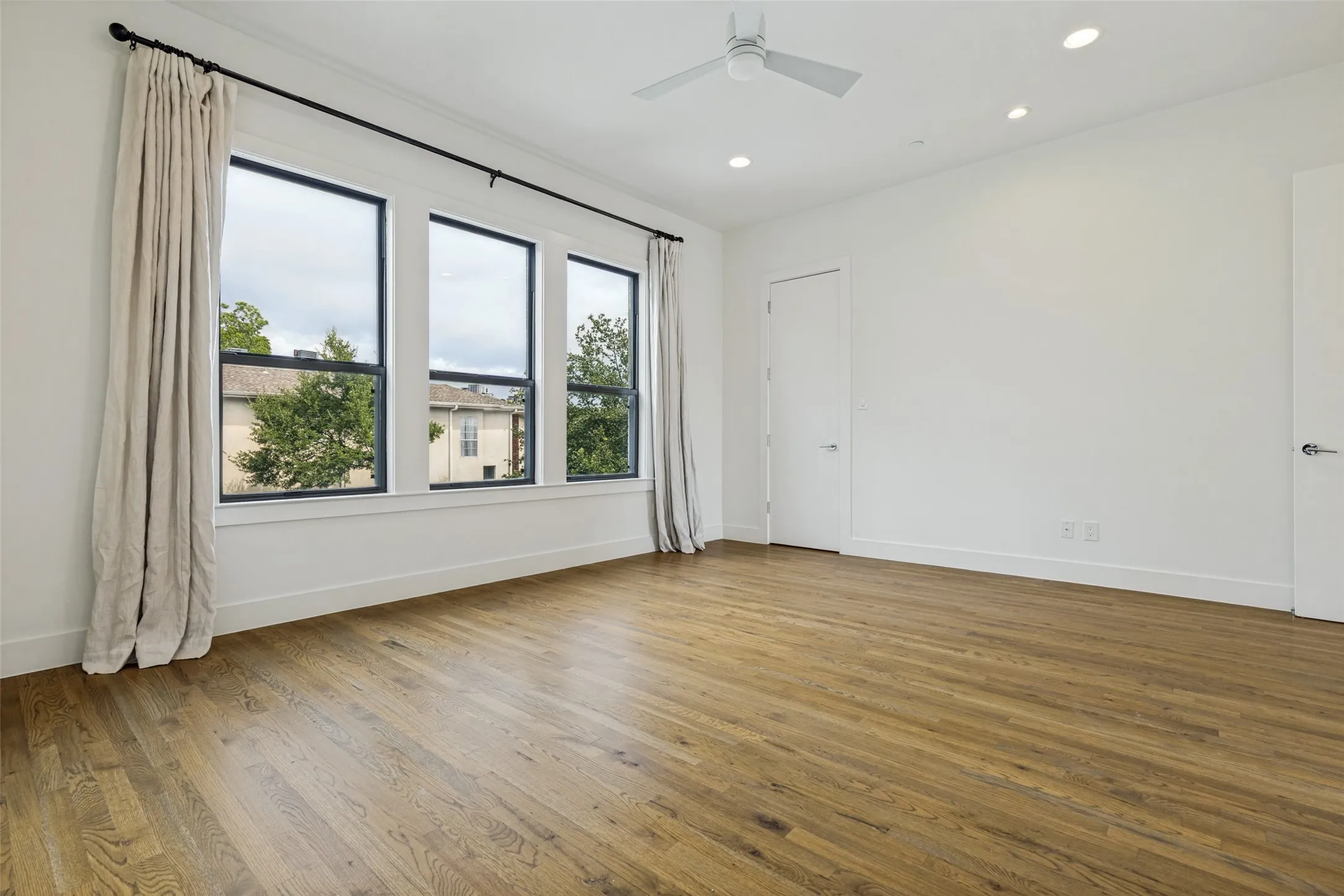 Spacious room featuring wood-finish flooring, a contemporary ceiling fan, and recessed lighting