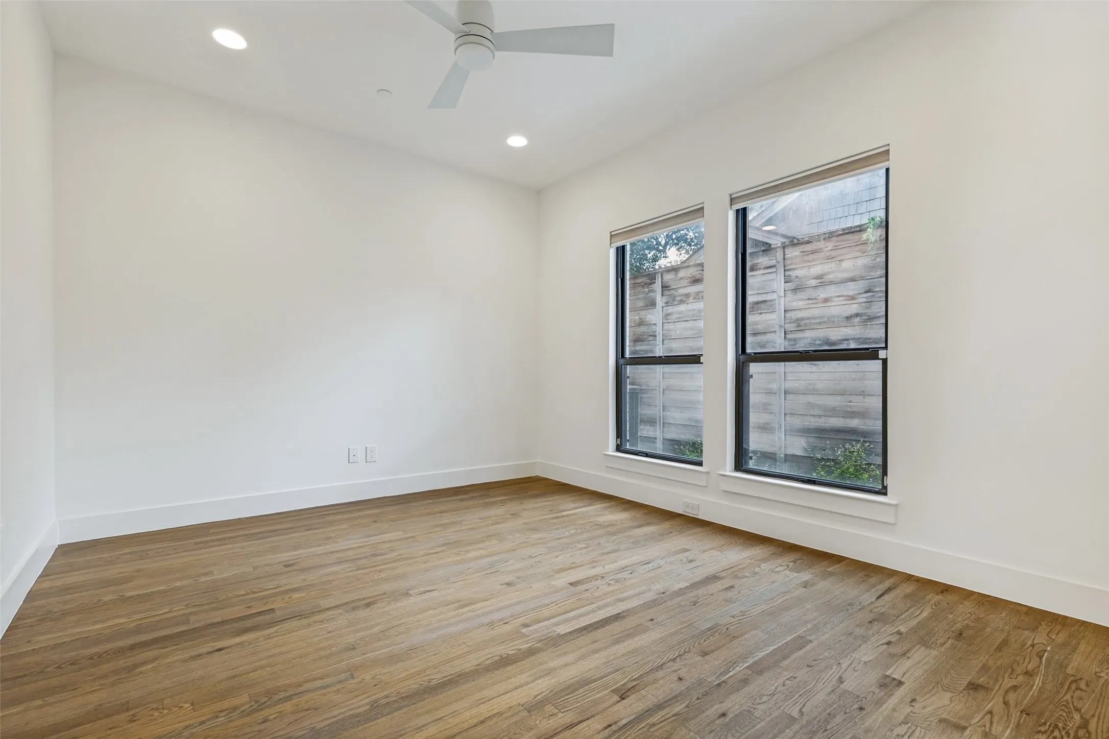Spacious room featuring wood-finish flooring, two large windows, a ceiling fan, and recessed lighting