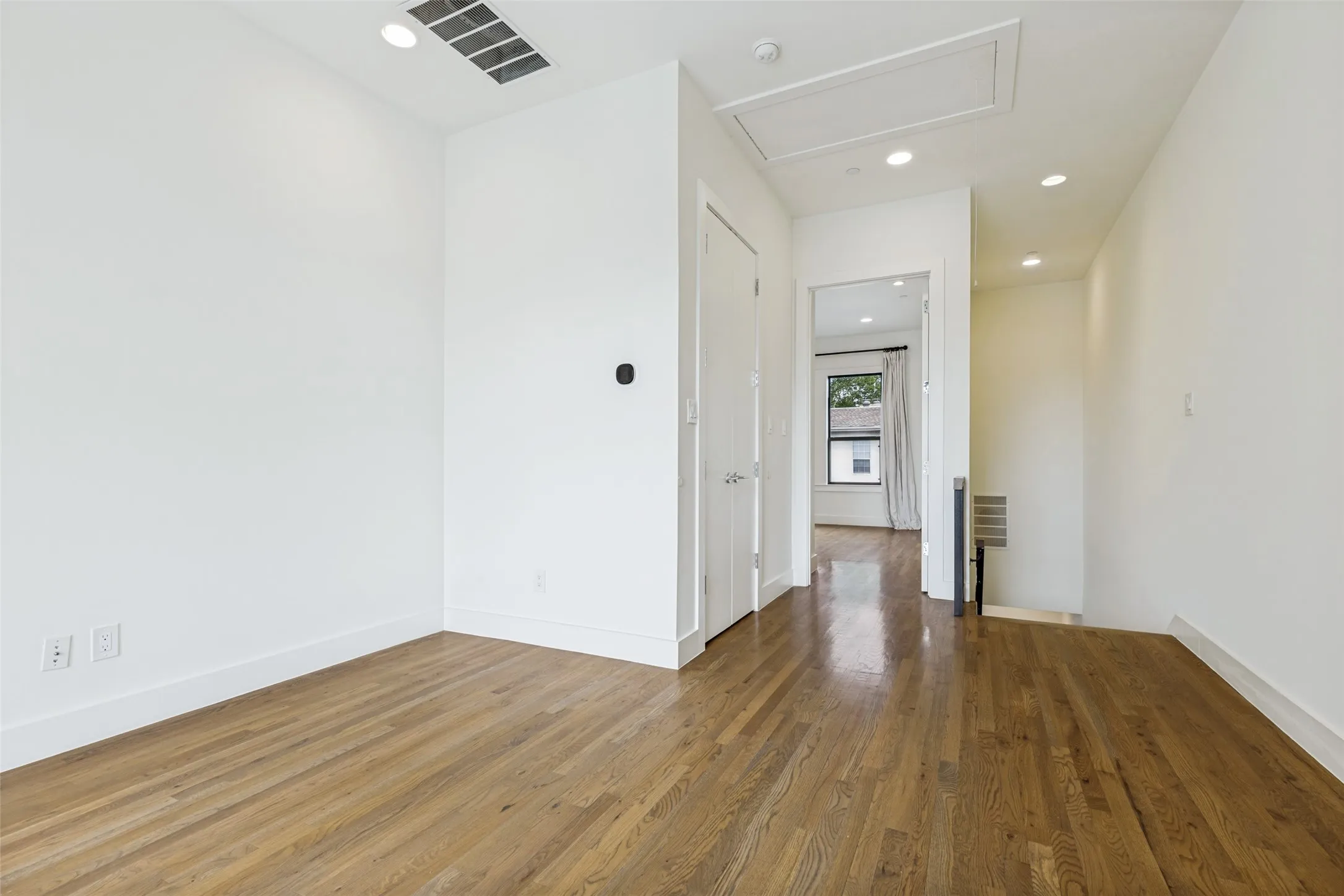 Hardwood flooring extends throughout this interior space, featuring white baseboards, recessed lighting, and a window providing natural light