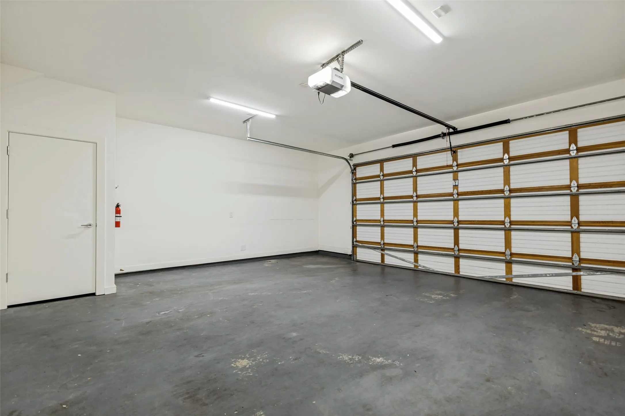 Spacious garage featuring a concrete floor, overhead lighting, an automatic garage door opener, and a side access door