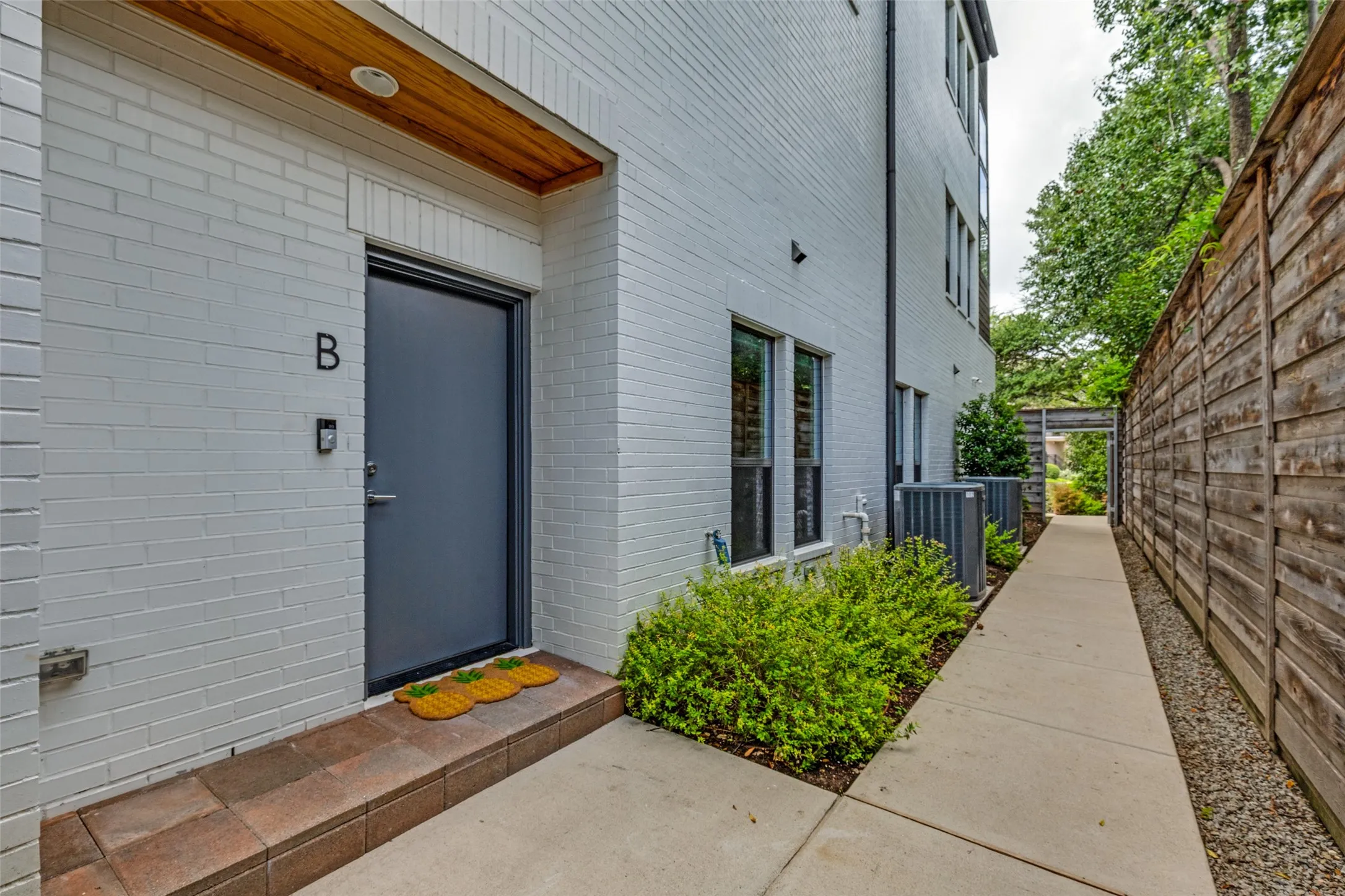 Modern white brick exterior with a dark entry door, wood-finish soffit, and a paver threshold