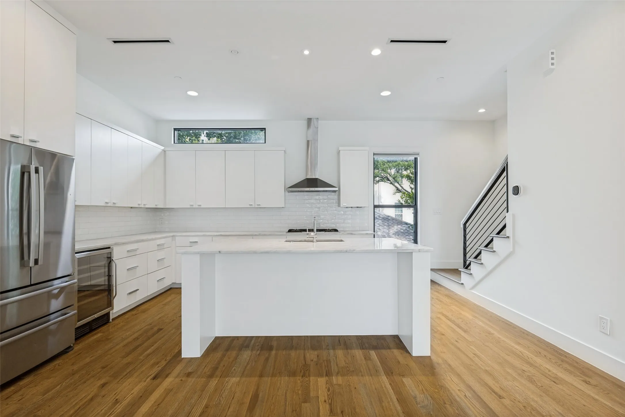 Modern kitchen featuring white cabinetry, stainless steel appliances, a center island with a sink, light-toned countertops, and wood-finish flooring