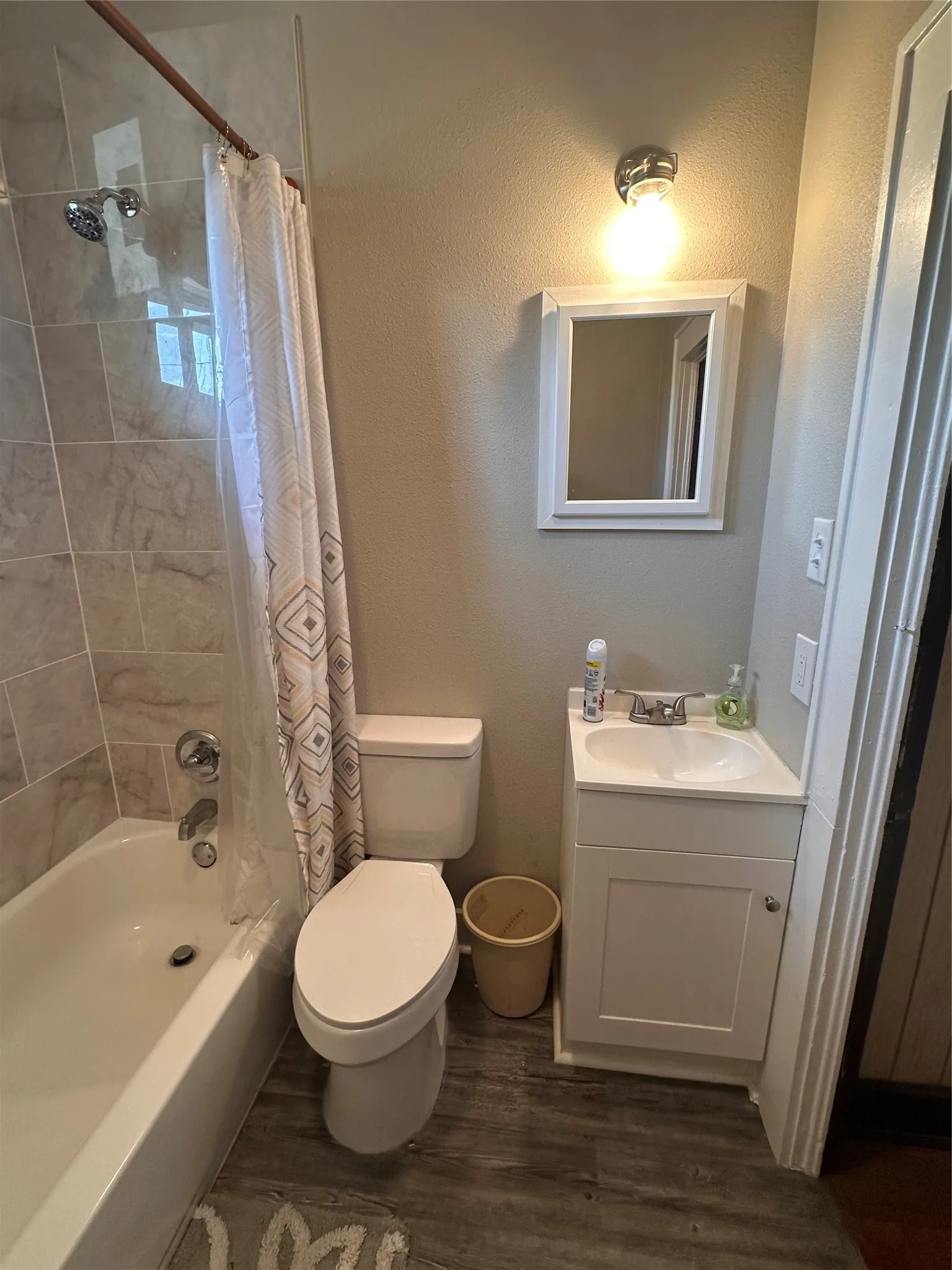 Bathroom featuring a white vanity with integrated sink, white toilet, and a bathtub with tiled surround
