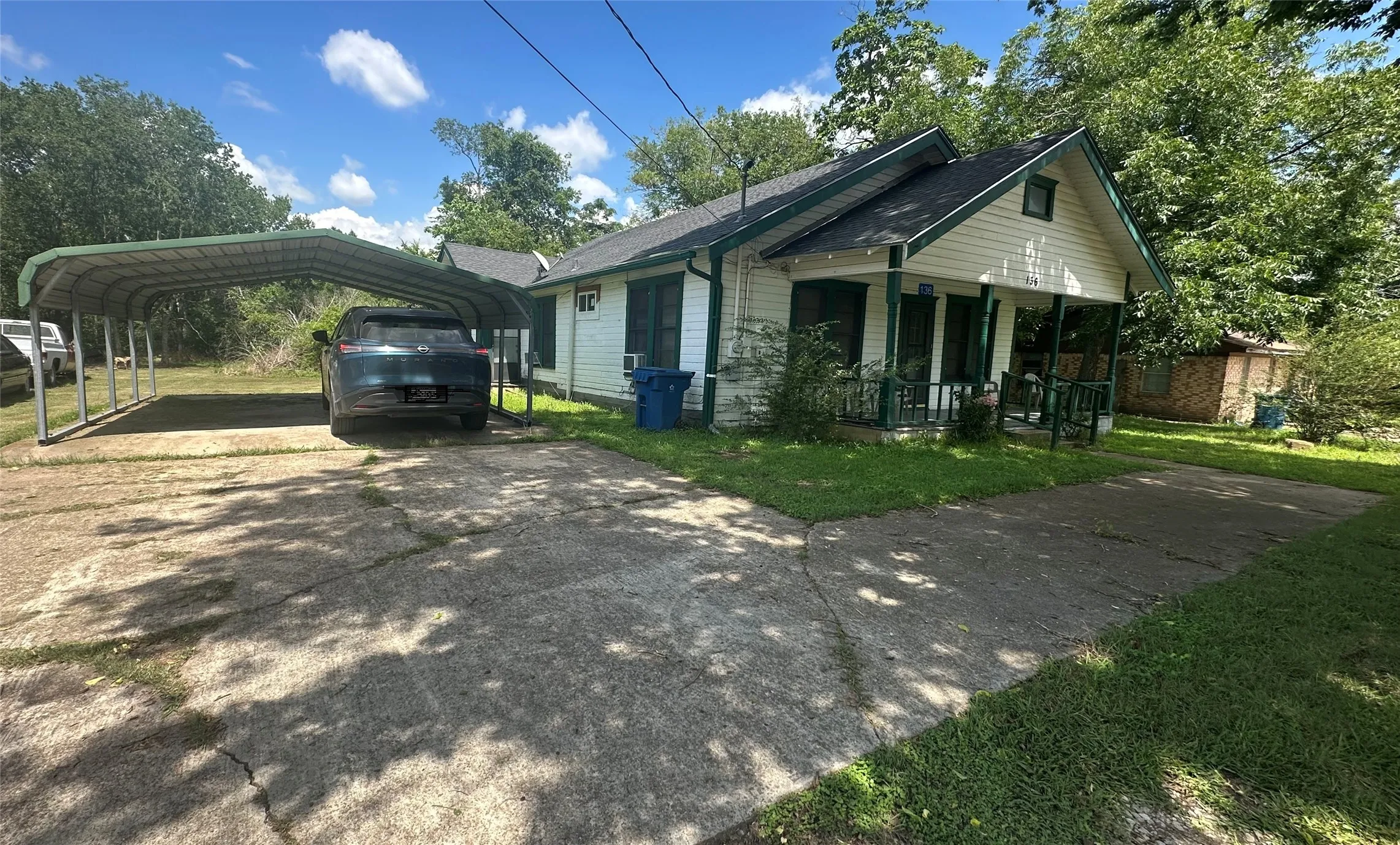 Front exterior featuring a metal carport structure, concrete driveway, and a covered porch with dark green accents