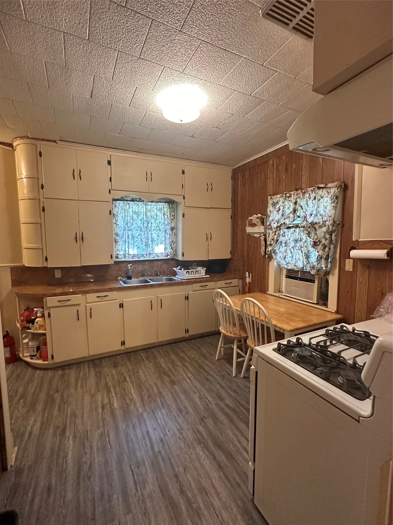 Kitchen featuring extensive cabinetry, laminate wood-finish flooring, a double basin sink, and a range with overhead ventilation