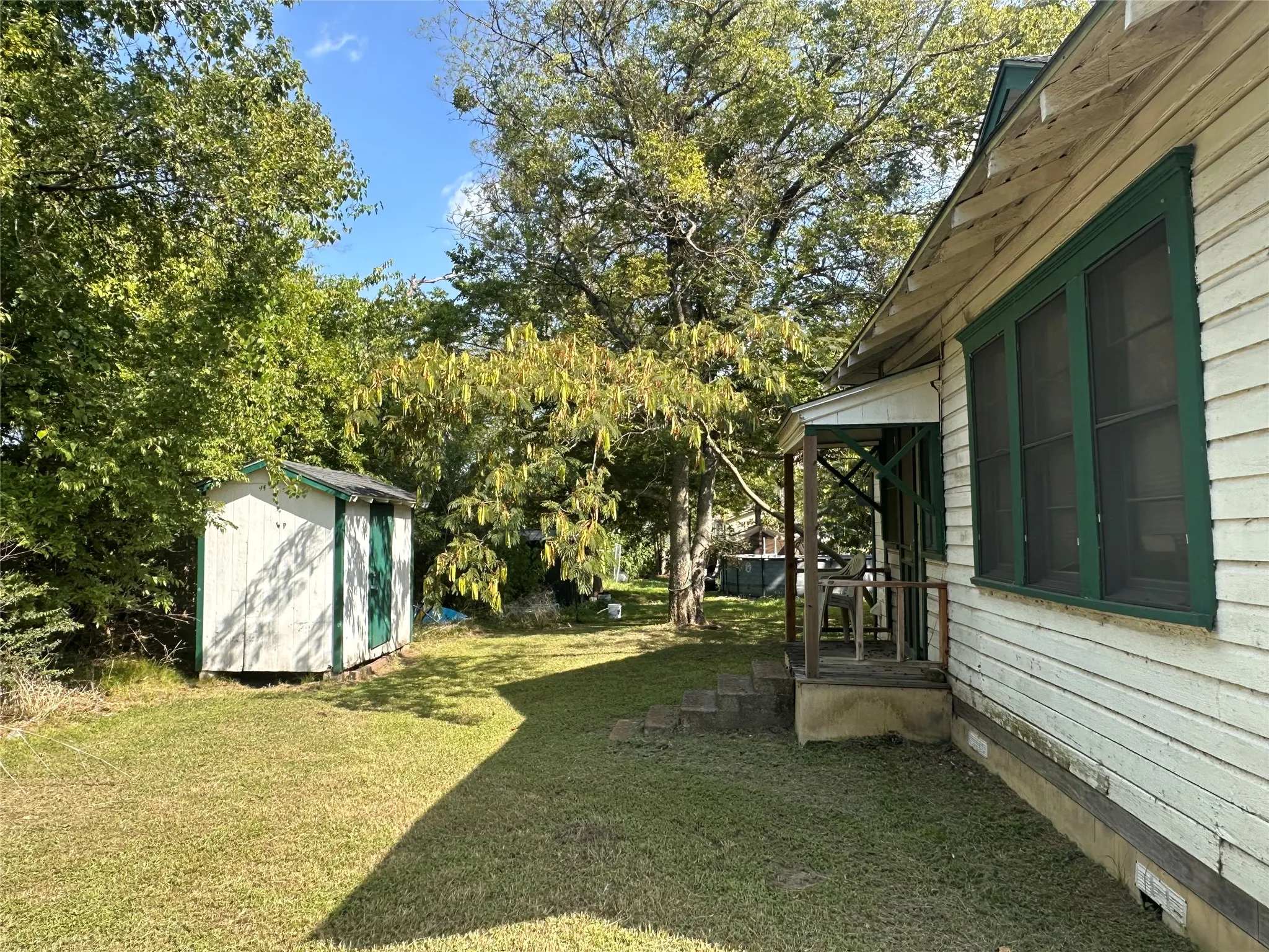 Expansive rear yard featuring a detached storage shed with a green trim, a covered porch, and mature trees