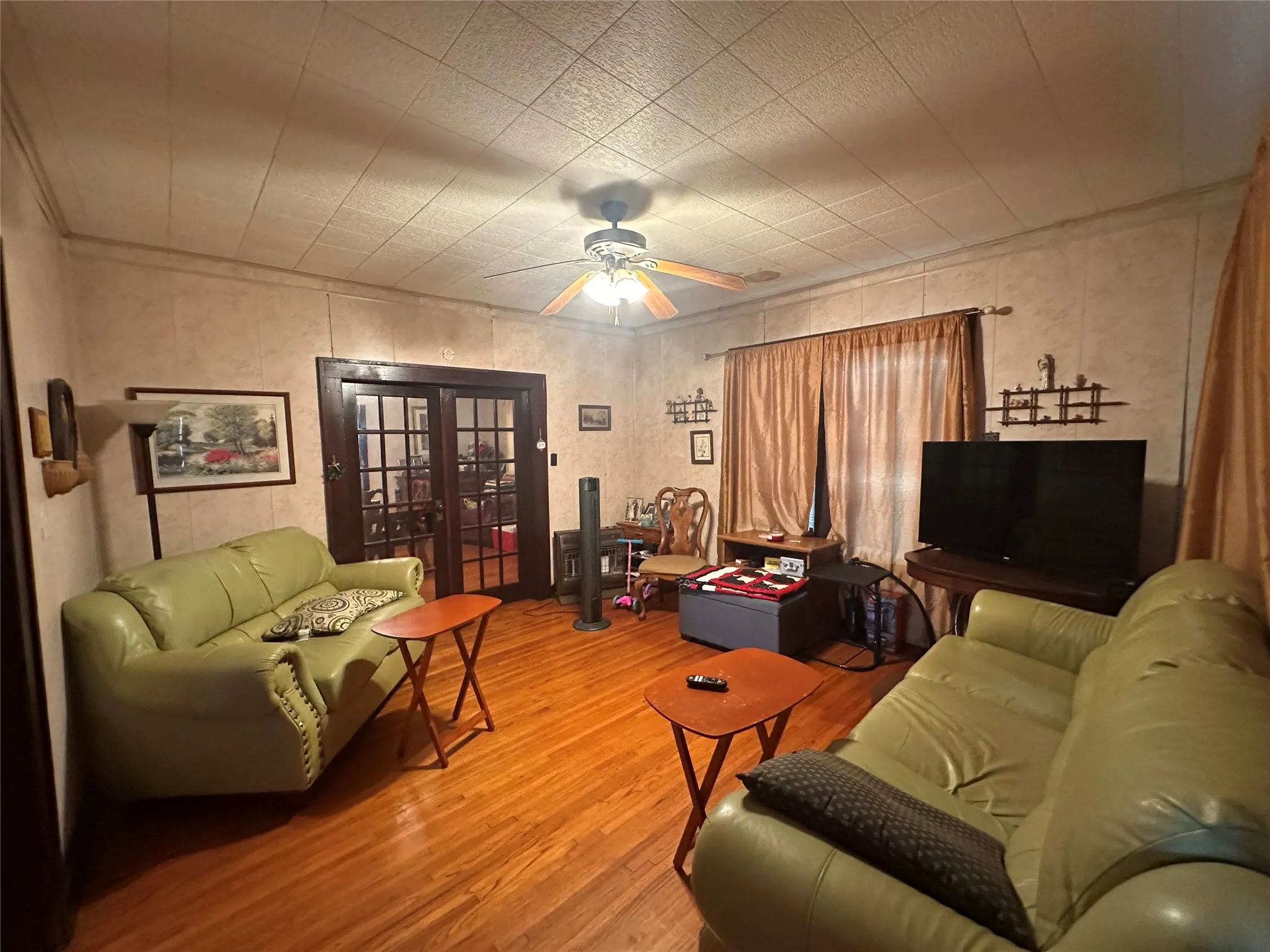 Living area featuring wood-finish flooring, a ceiling fan with integrated lighting, and paneled walls