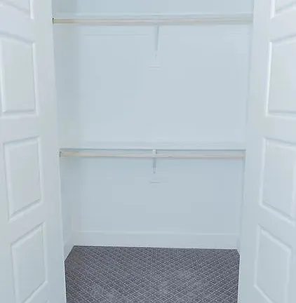 Spacious closet featuring two hanging rods, light-toned wall paint, and patterned gray carpeting
