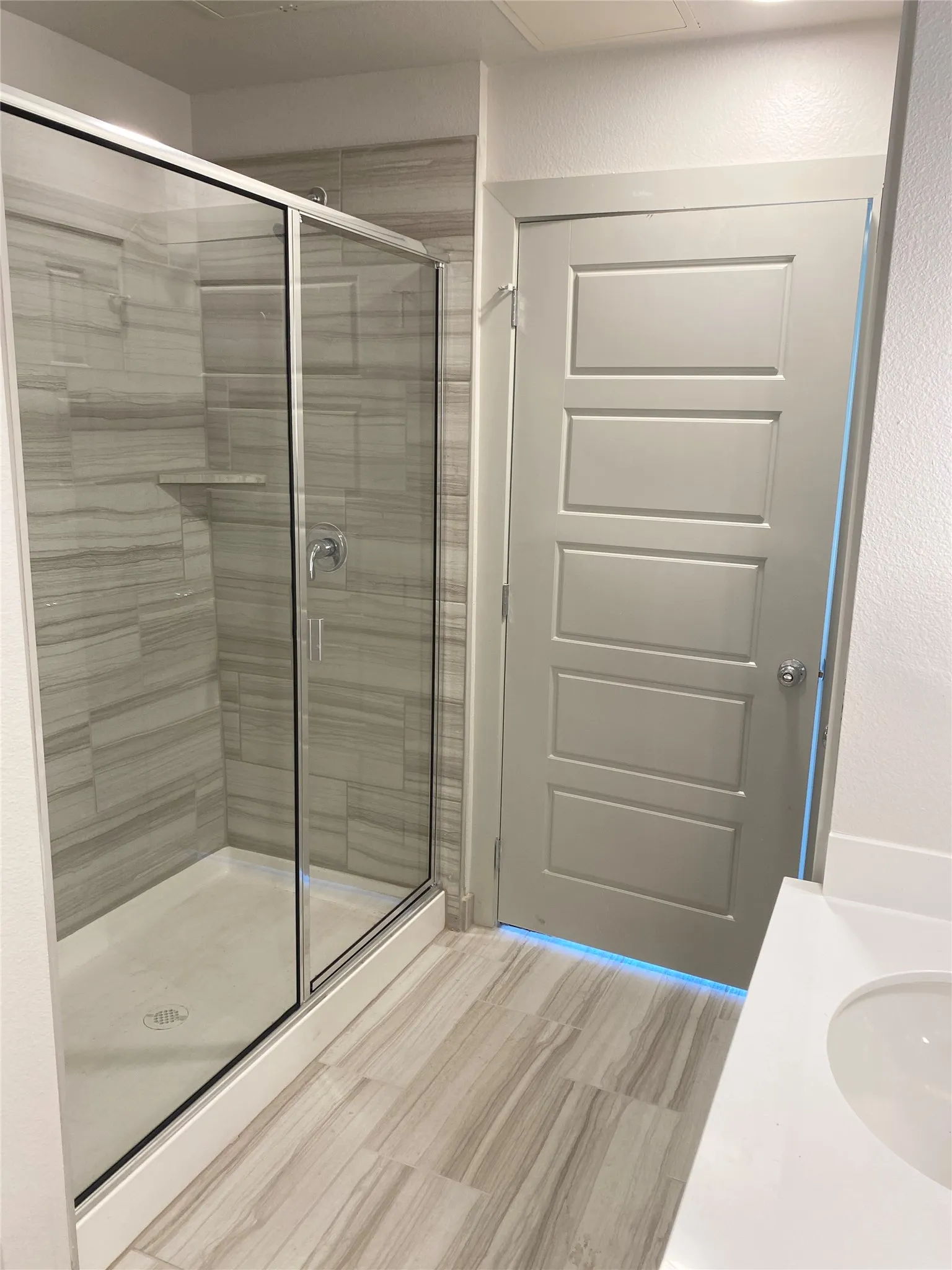 Glass-enclosed shower with horizontal tile surround and integrated shelf, complemented by wood-finish flooring