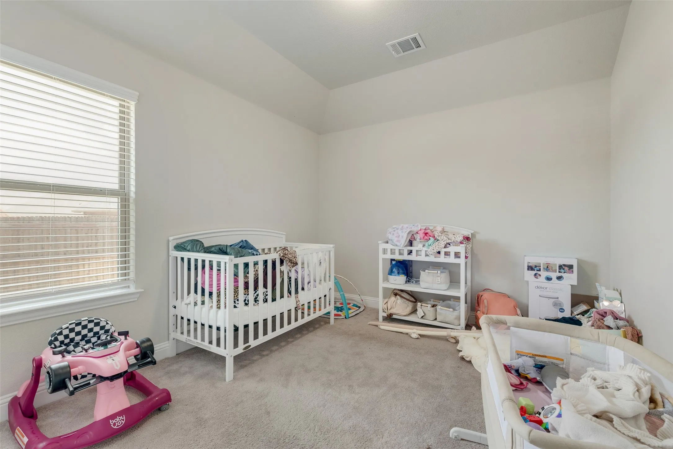 Carpeted bedroom with multiple windows, a crib, and vaulted ceiling