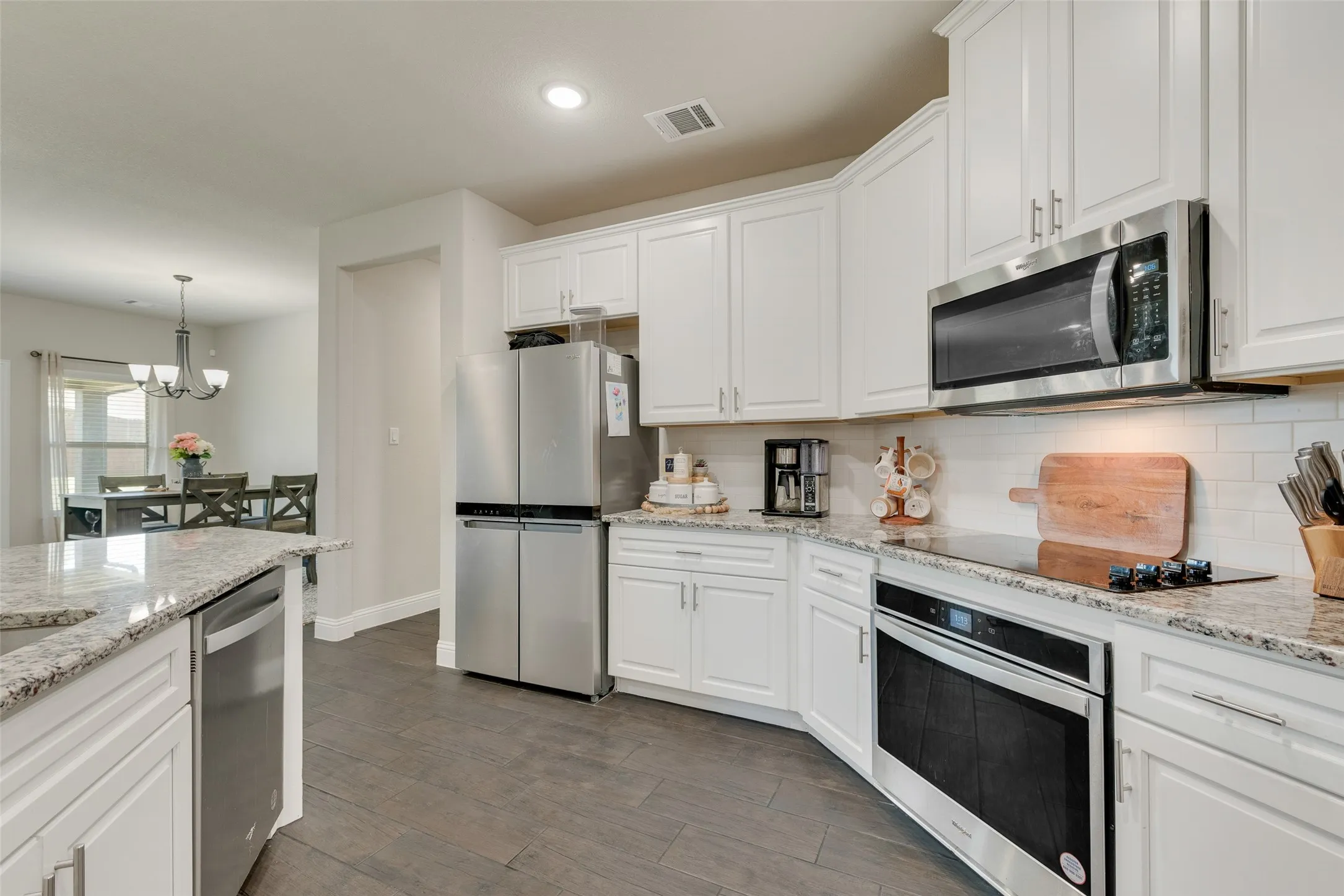 Kitchen with appliances with stainless steel finishes, a chandelier, white cabinets, backsplash, and dark wood-style floors