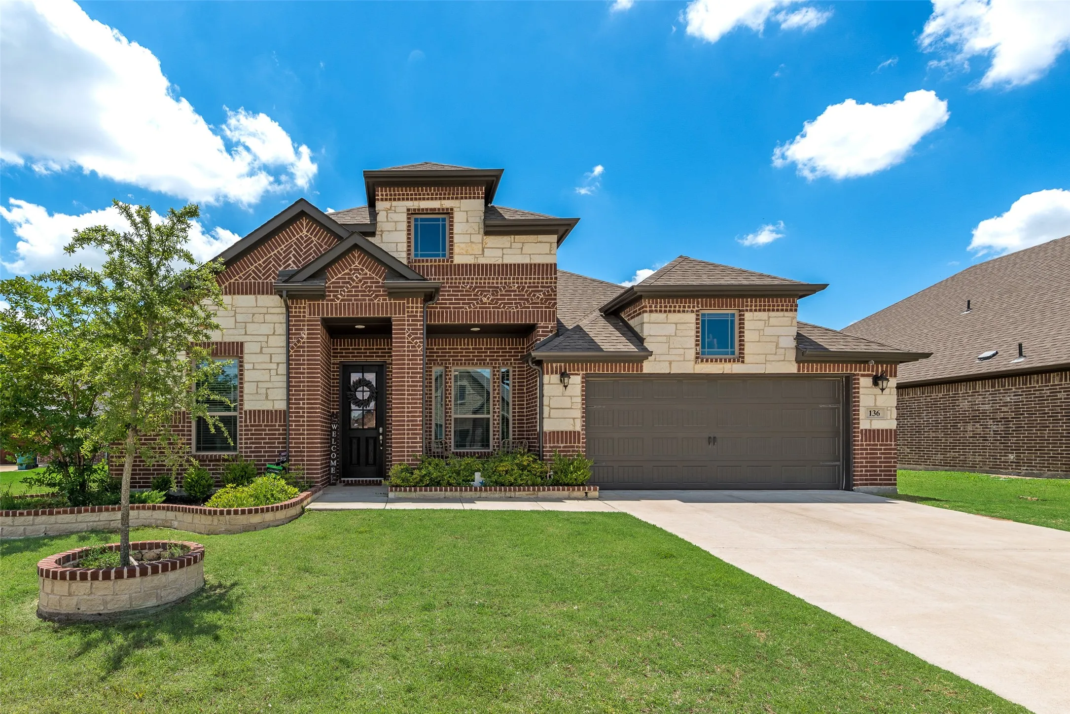View of front of home featuring brick siding, an attached garage, driveway, a shingled roof, and stone siding