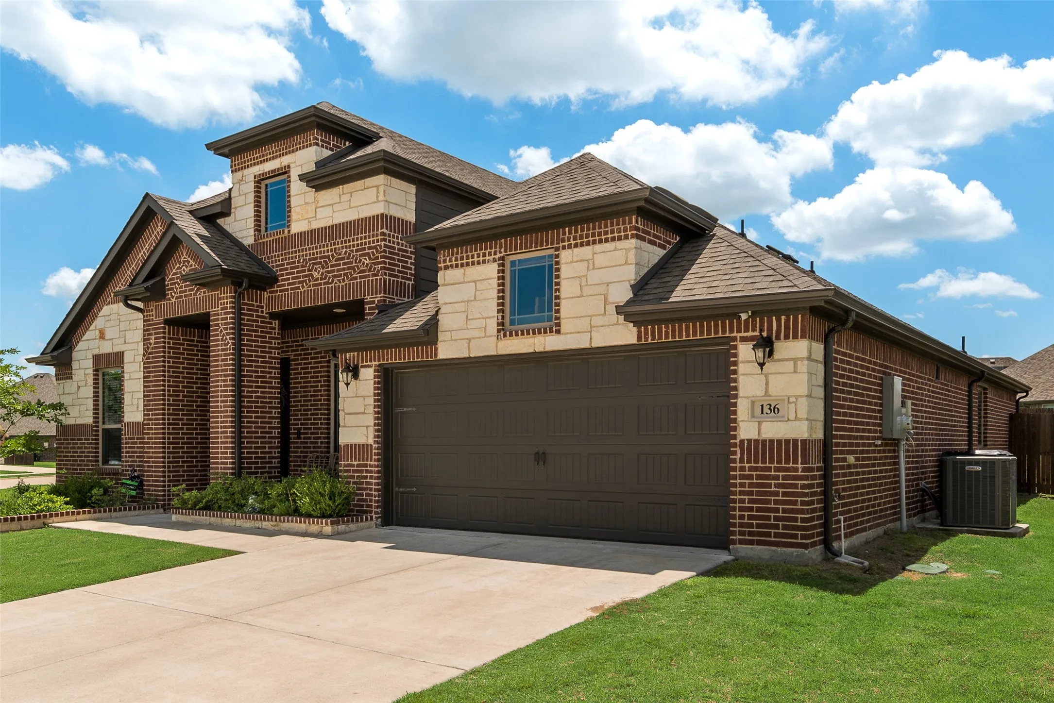 View of front of home with stone siding, roof with shingles, concrete driveway, brick siding, and a front yard
