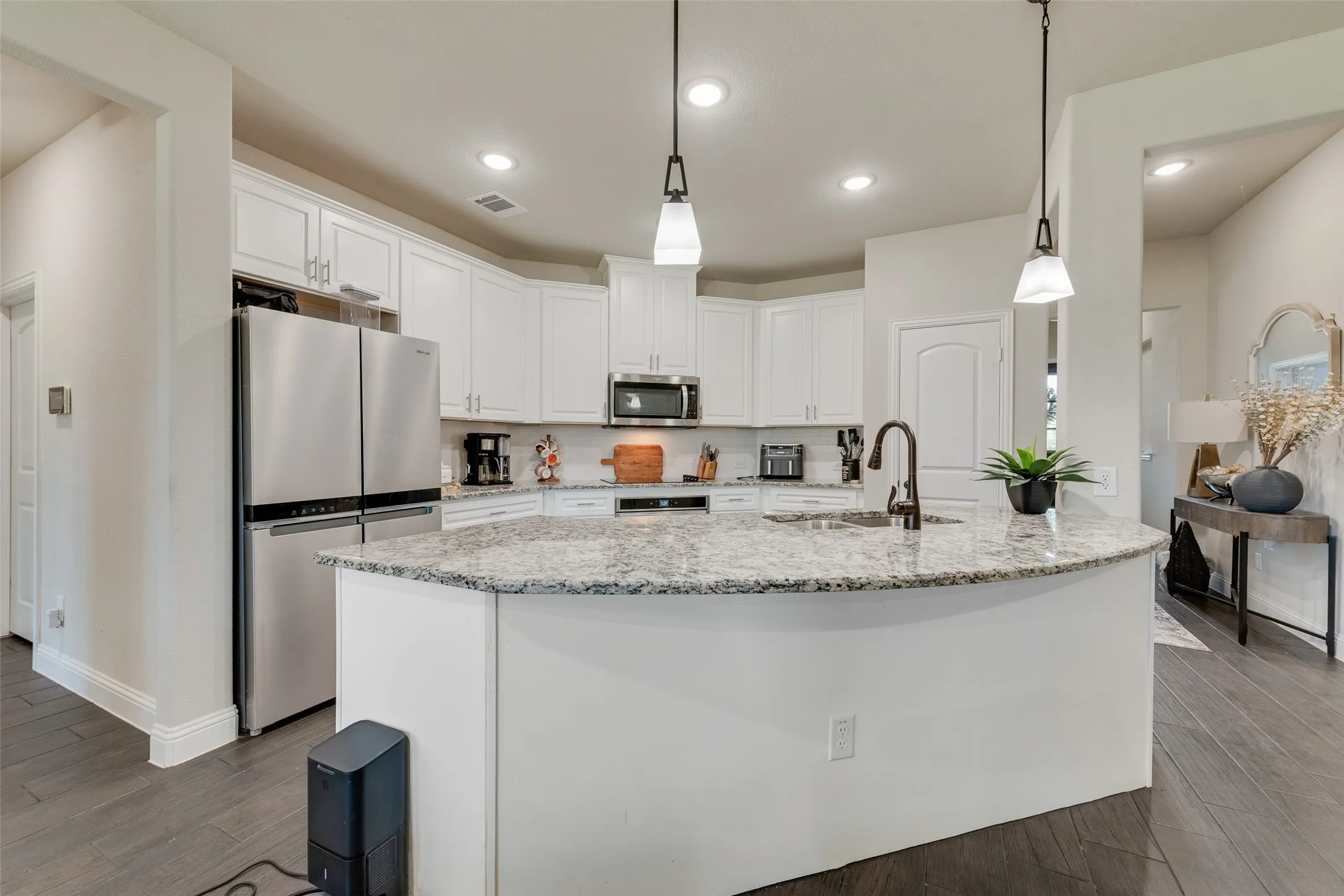 Kitchen featuring appliances with stainless steel finishes, white cabinets, dark wood-type flooring, a kitchen island with sink, and light stone countertops