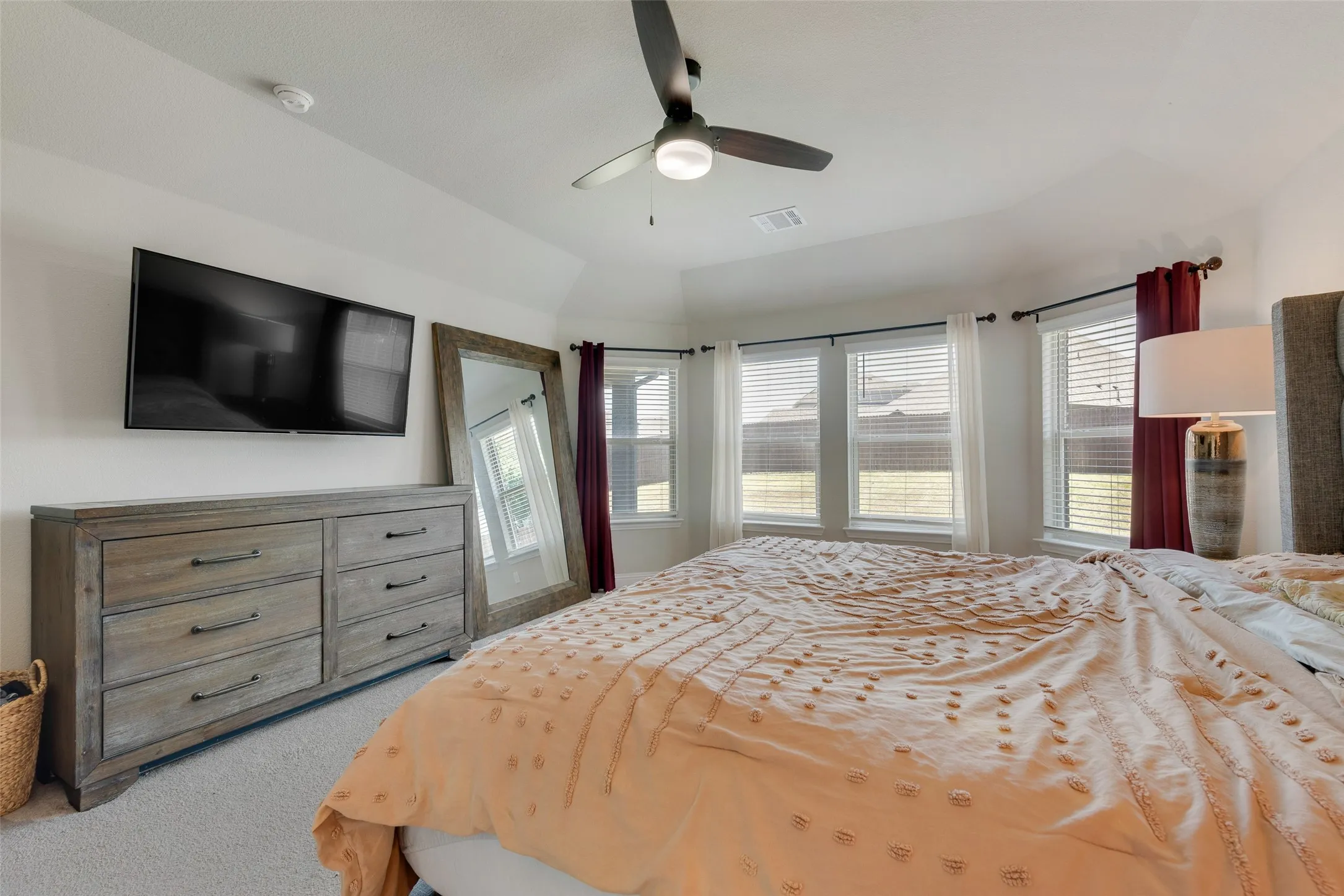 Carpeted bedroom featuring multiple windows, ceiling fan, and vaulted ceiling