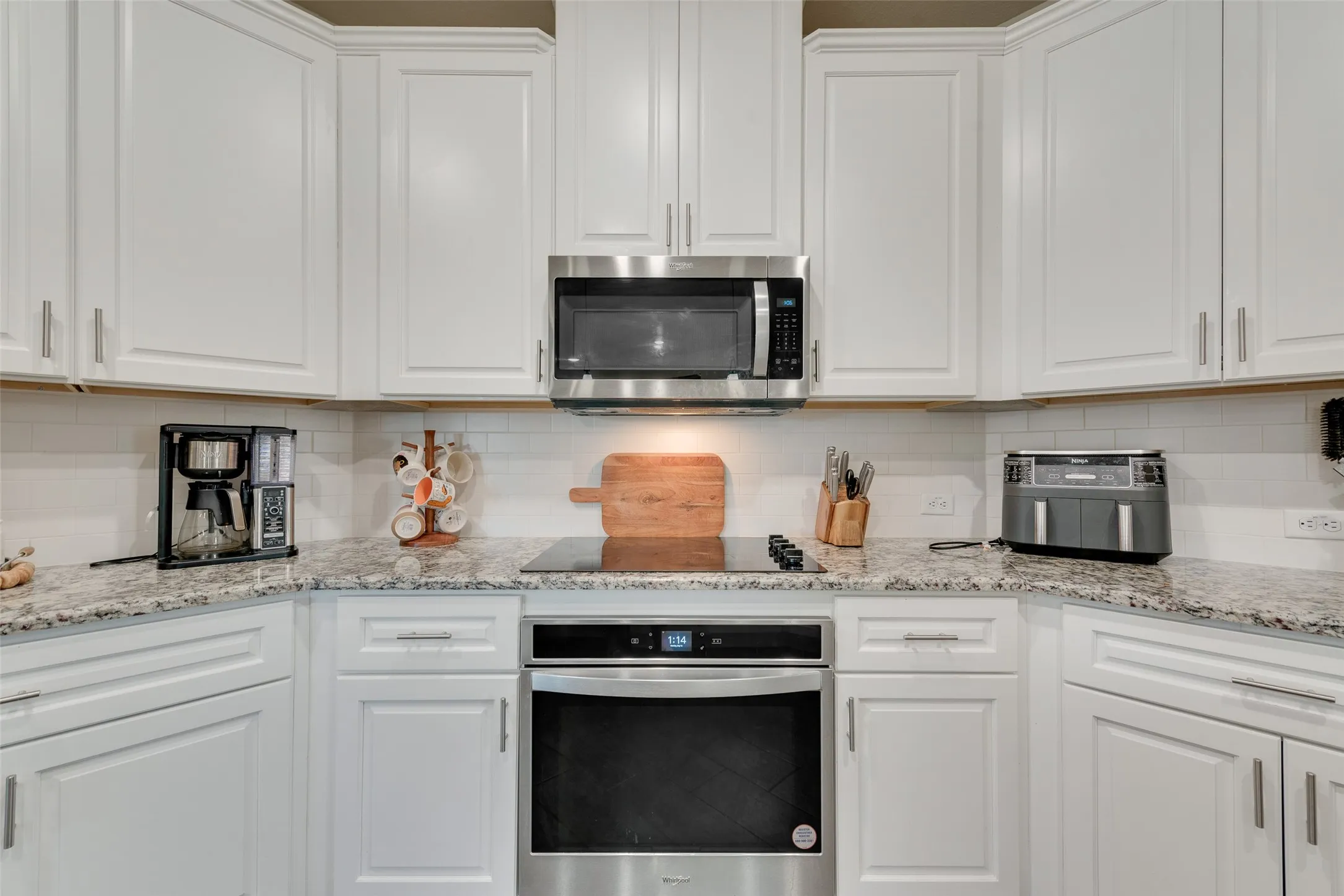 Kitchen featuring appliances with stainless steel finishes, white cabinetry, tasteful backsplash, and light stone counters