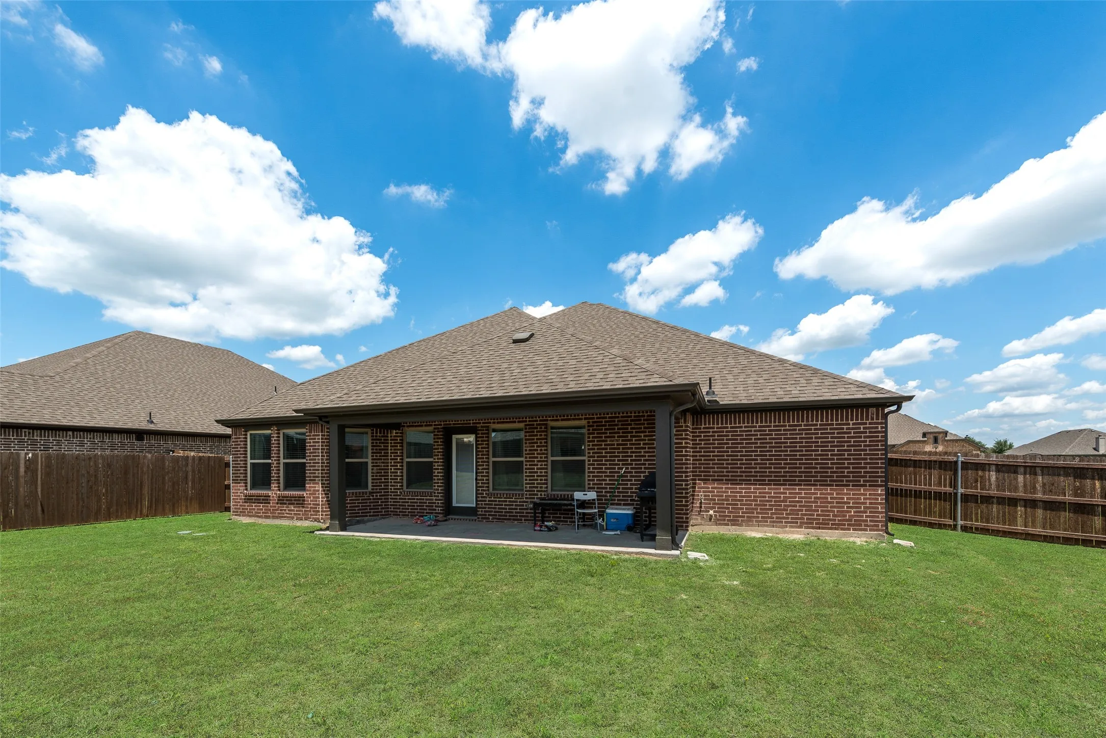 Rear view of house with brick siding, a shingled roof, a fenced backyard, and a patio area