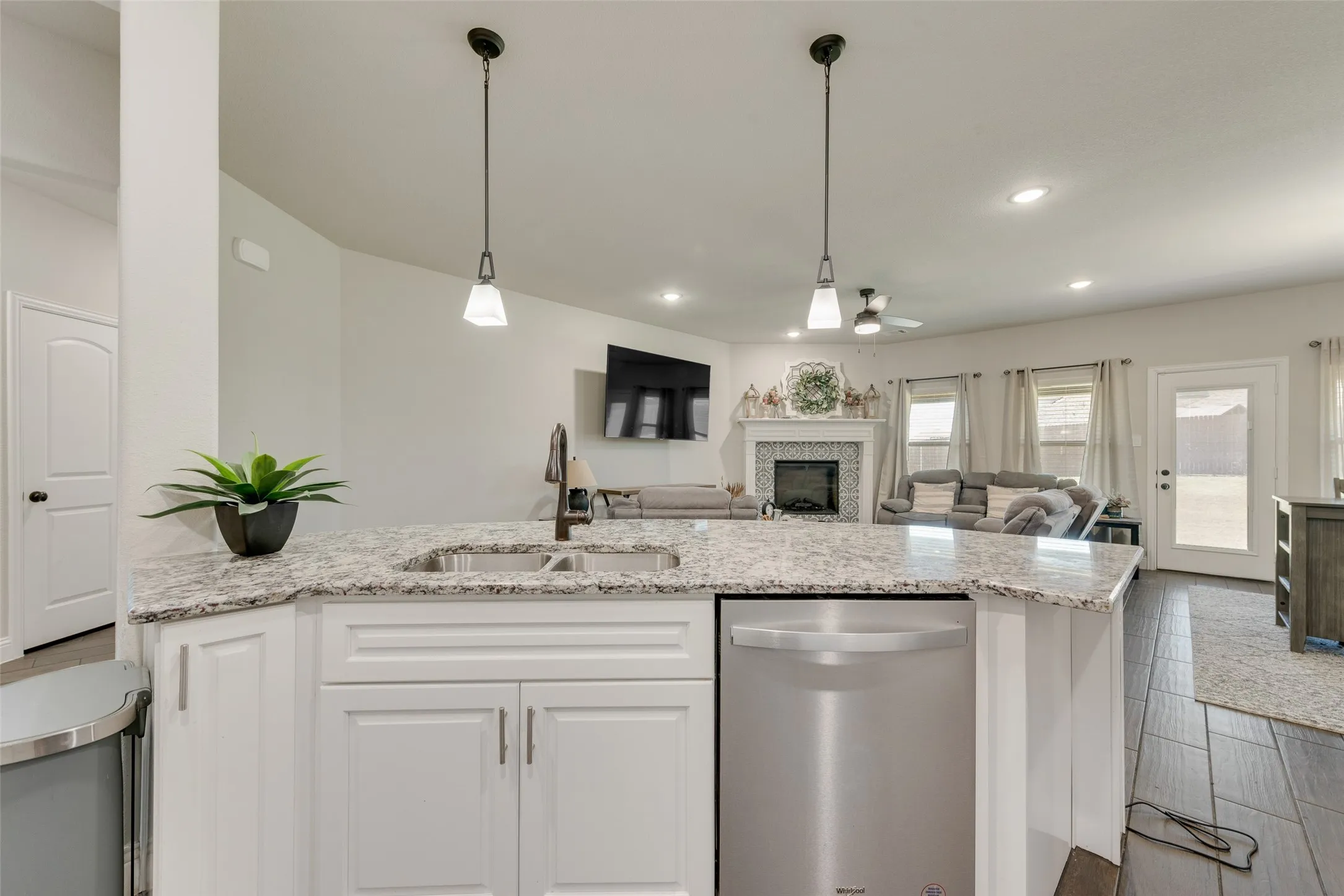 Kitchen featuring stainless steel dishwasher, recessed lighting, a tile fireplace, white cabinets, and light stone counters