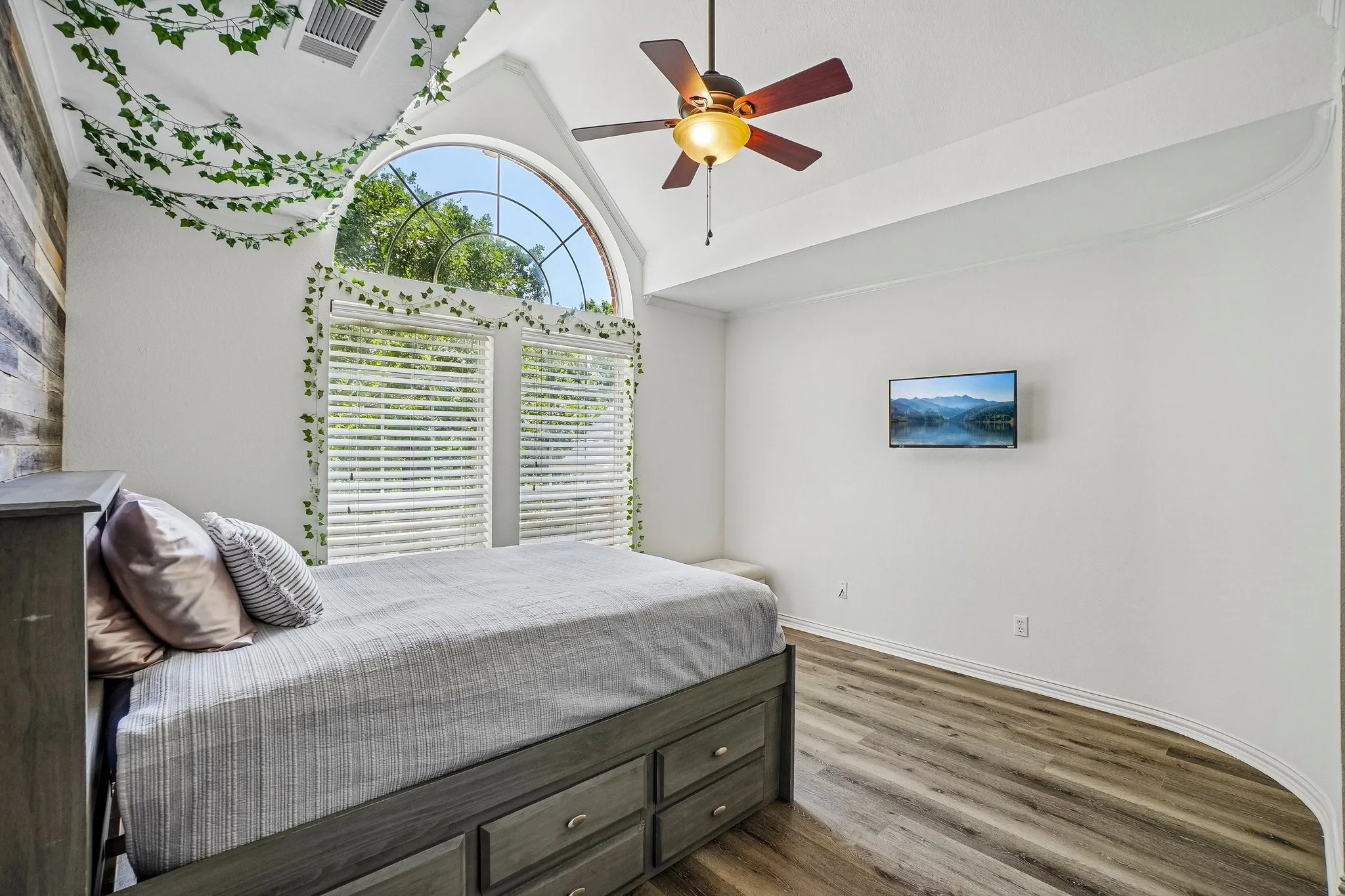 Vaulted ceiling room featuring a large arched window, and a ceiling fan with integrated lighting