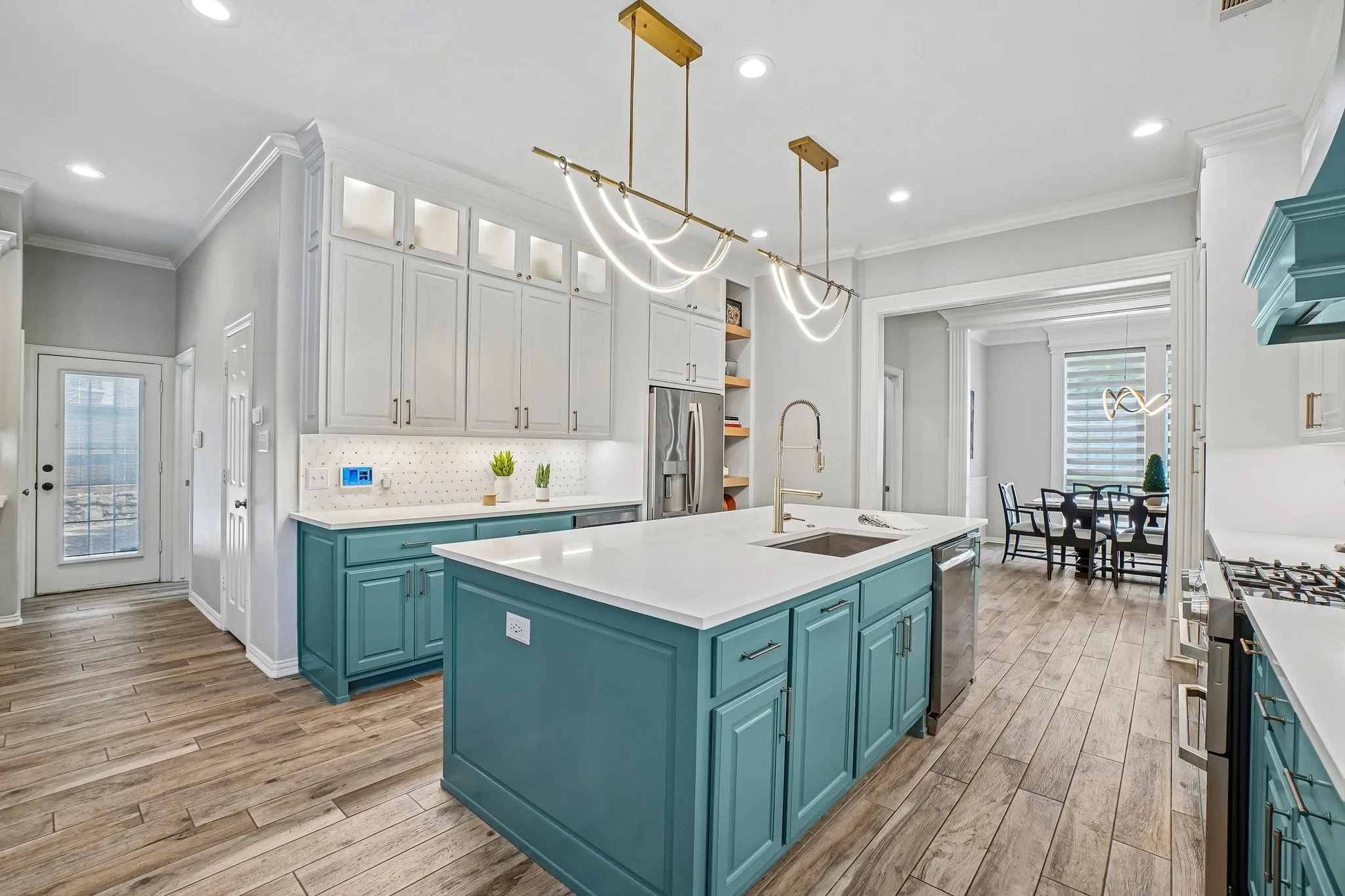 Gourmet kitchen with a large center island, contrasting cabinetry featuring both white upper and teal lower cabinets, stainless steel appliances, and wood-like tile flooring