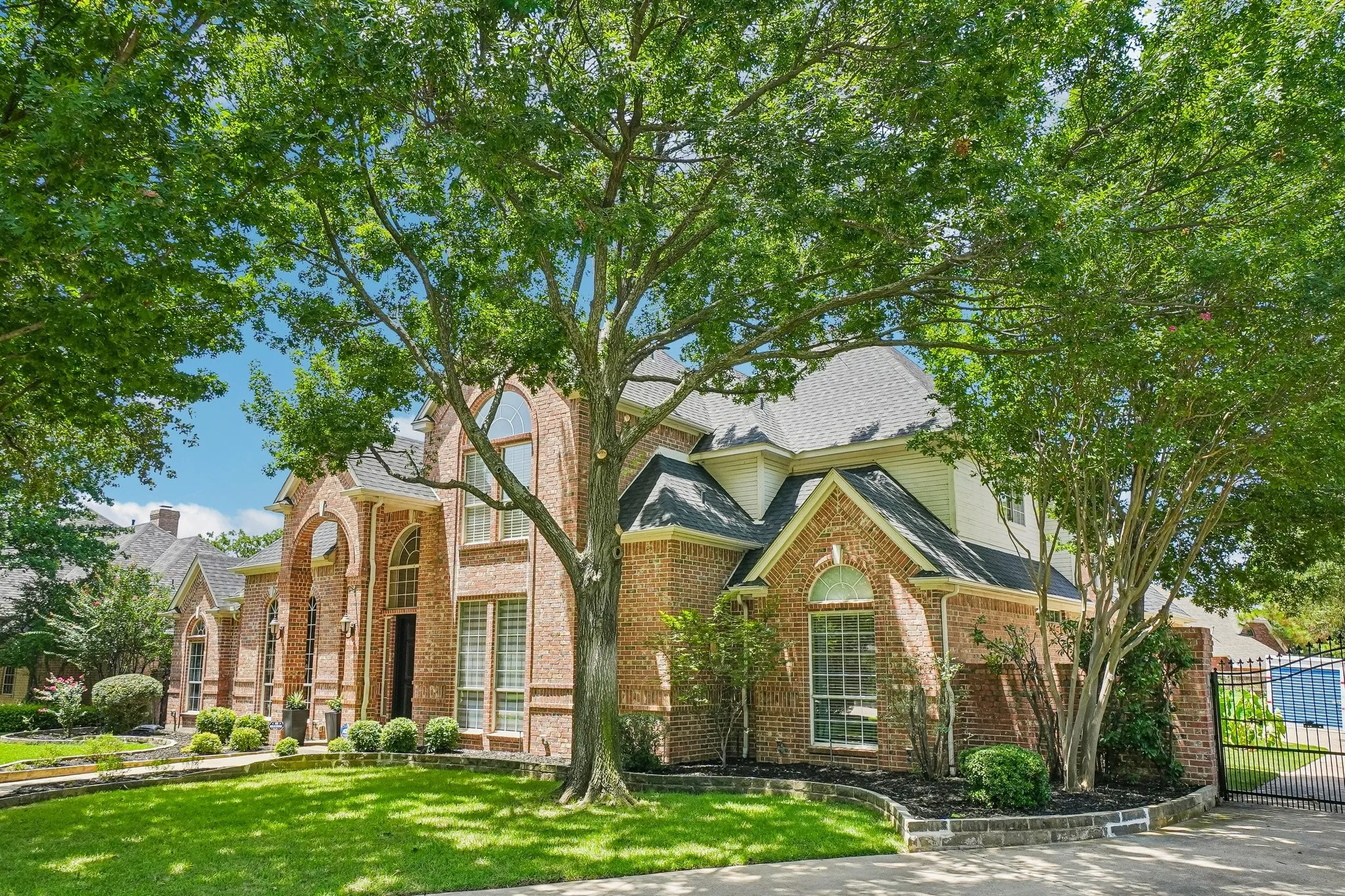 Brick home with arched windows and majestic Oak Trees.  Security gate leads to the three car garage