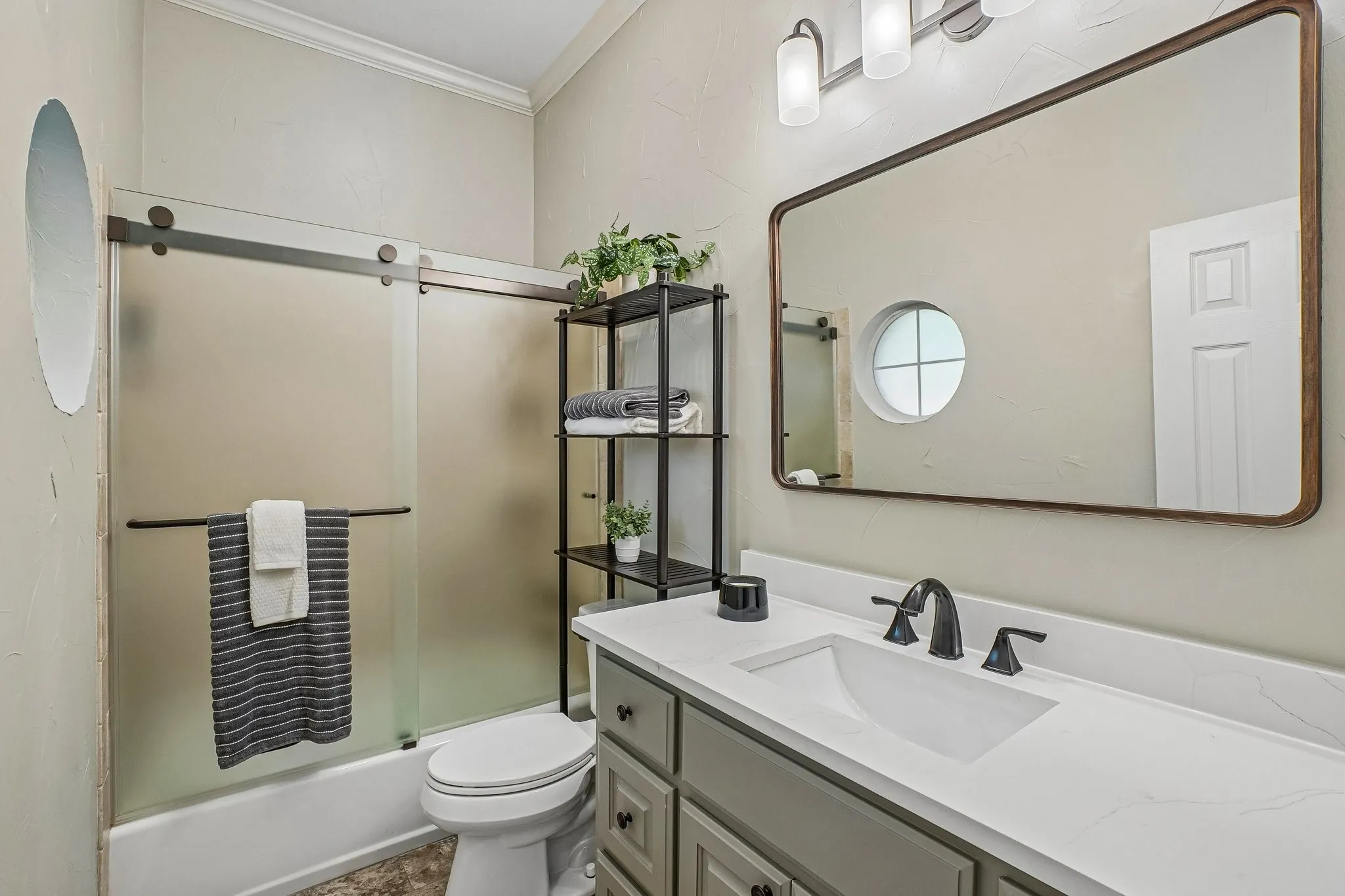 Bathroom off the guest suite featuring a single vanity with gray cabinetry and a white counter-top, a black matte faucet, a rectangular framed mirror, and a tub with frosted sliding glass doors