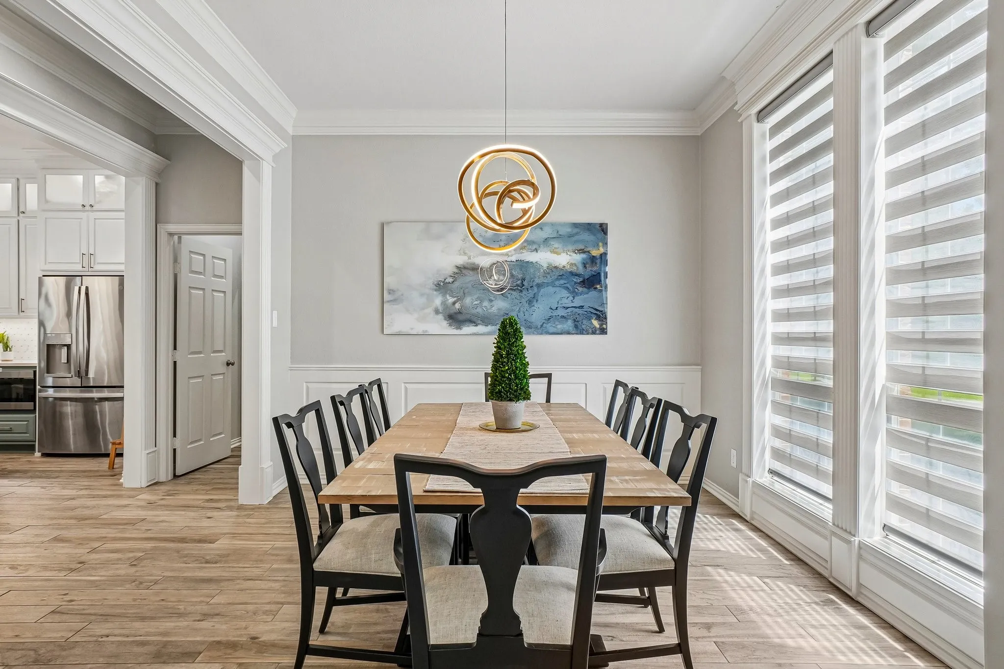 Dining room featuring wood-look tile flooring, wainscoting, and crown molding.  Window coverings are remotely controlled.