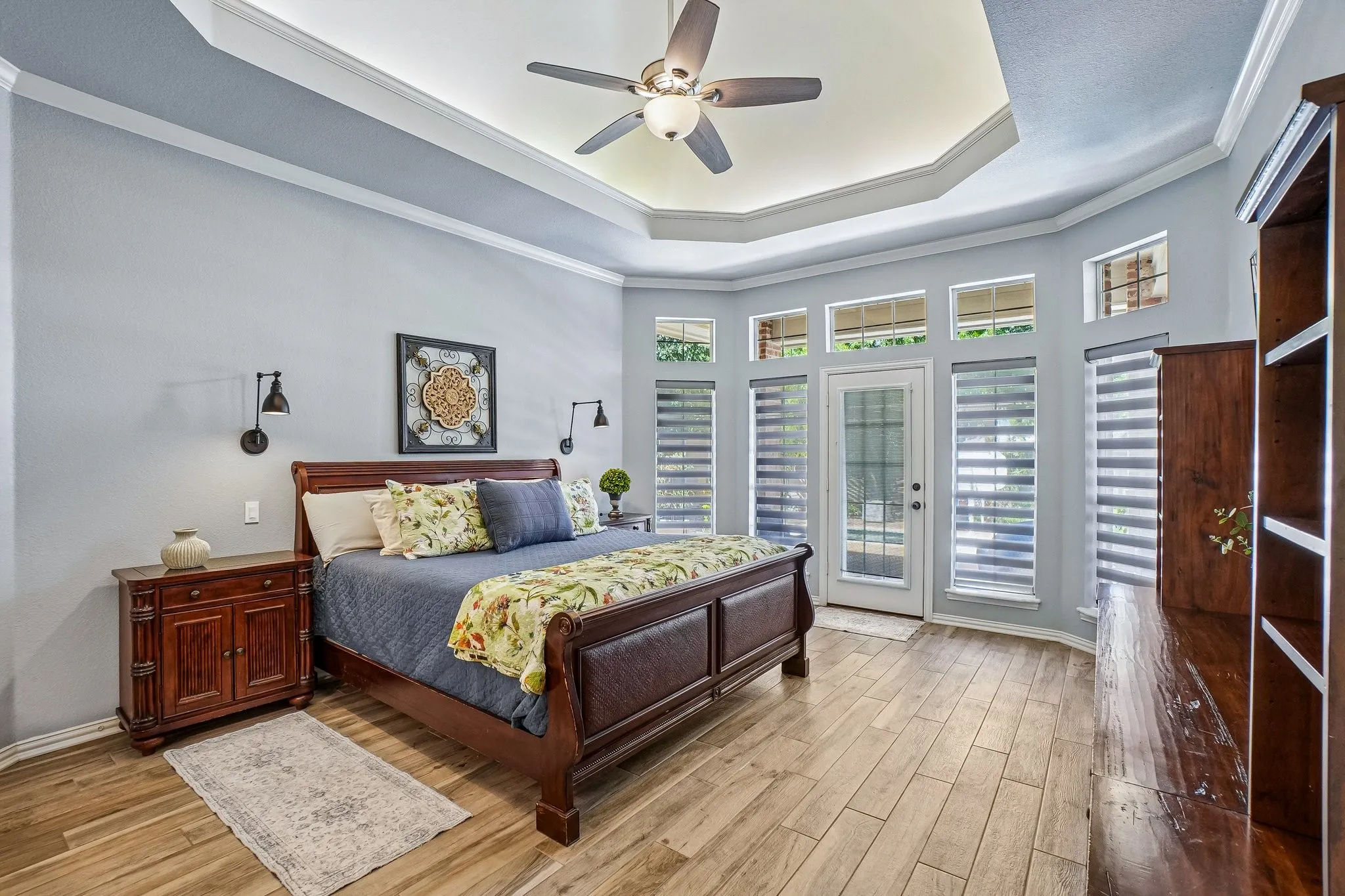 Room featuring wood-look tile flooring, a tray ceiling with illumination and crown molding, and a ceiling fan.  Easy access to the patio area.