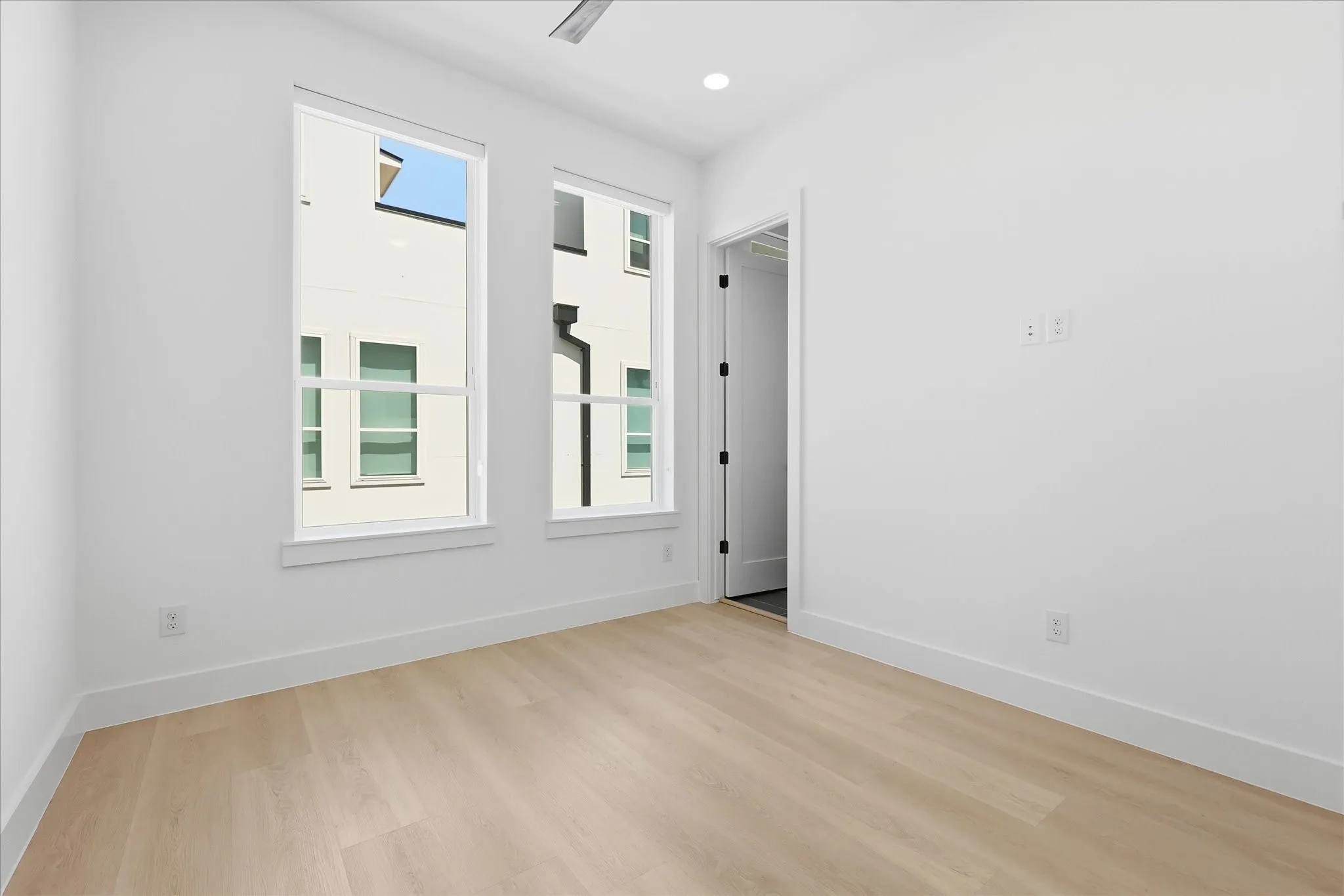 Bright room featuring two large sash windows, light wood-finish flooring, white baseboards, and a ceiling fan
