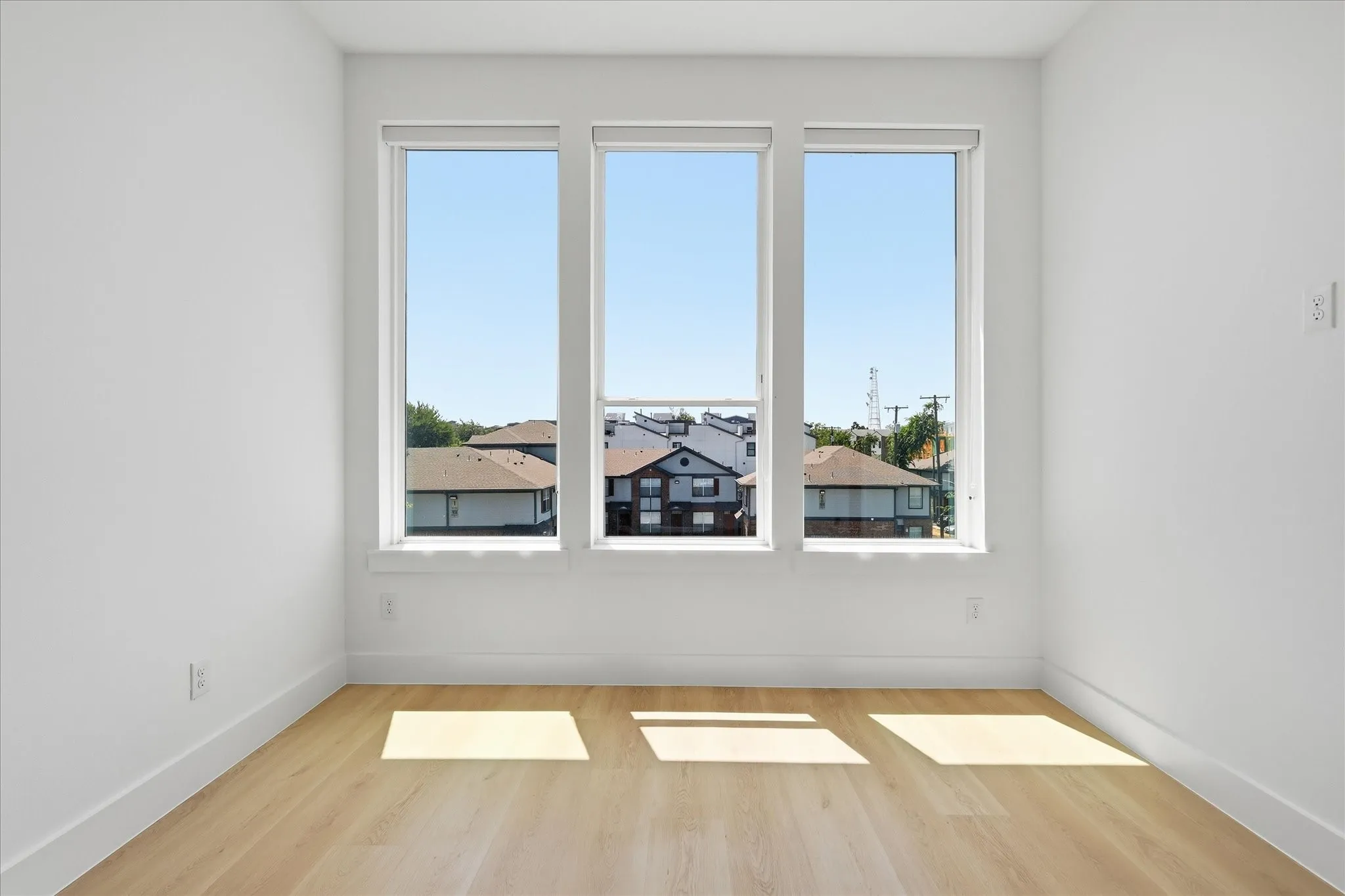 Bright interior space featuring three large vertical windows, light wood-finish flooring, white walls, and white baseboards