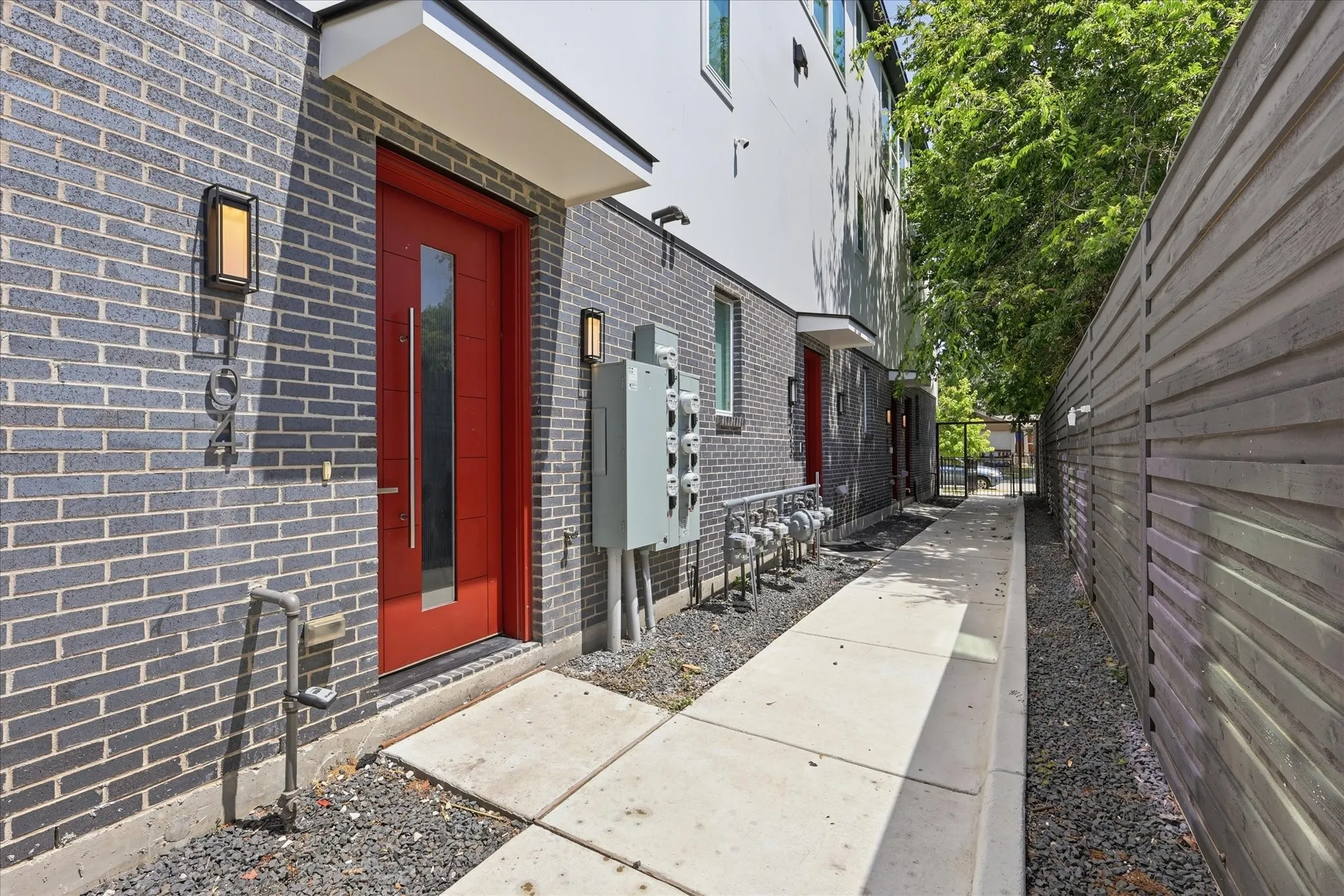Contemporary exterior featuring dark gray brick, a vibrant red entry door with vertical glass insert, and a flat white awning