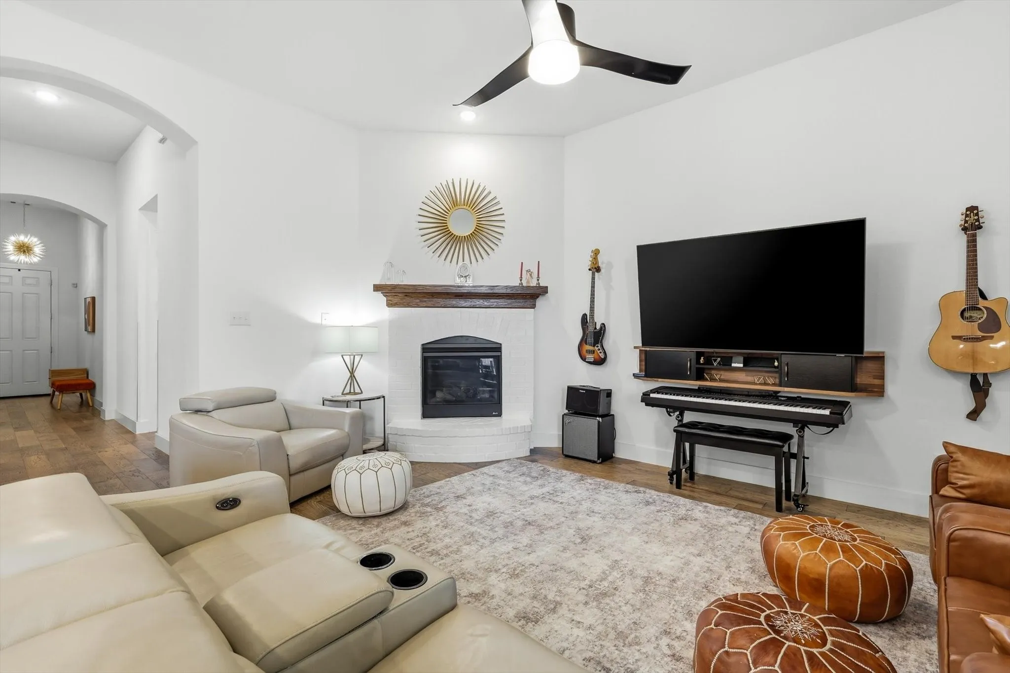 Living space featuring a whitewashed brick fireplace with a wood mantle, a modern black ceiling fan, wood-finish flooring, and an arched entryway