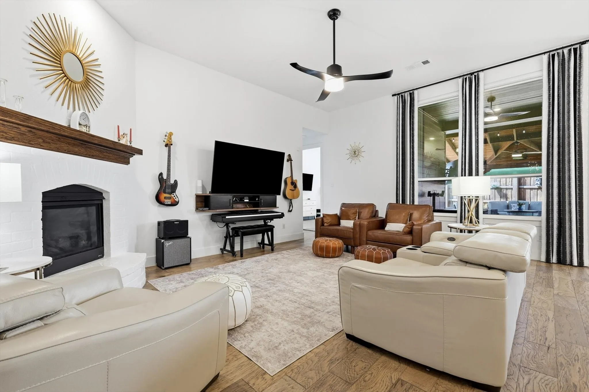 Living area featuring a white brick fireplace with a wood mantel, wood-finish flooring, and a ceiling fan