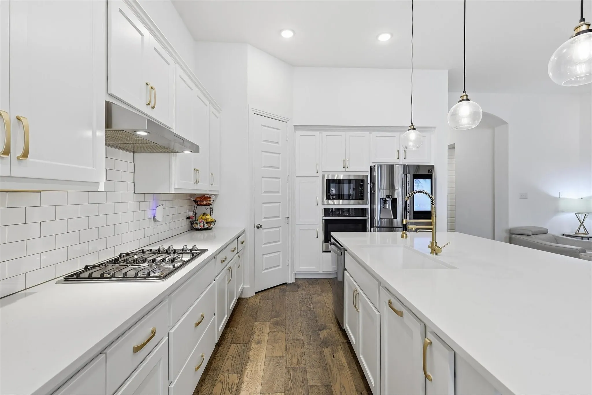 Modern kitchen featuring white cabinetry, light countertops, wood-finish flooring, a built-in stainless steel oven and microwave, and a gas cooktop with an overhead range hood