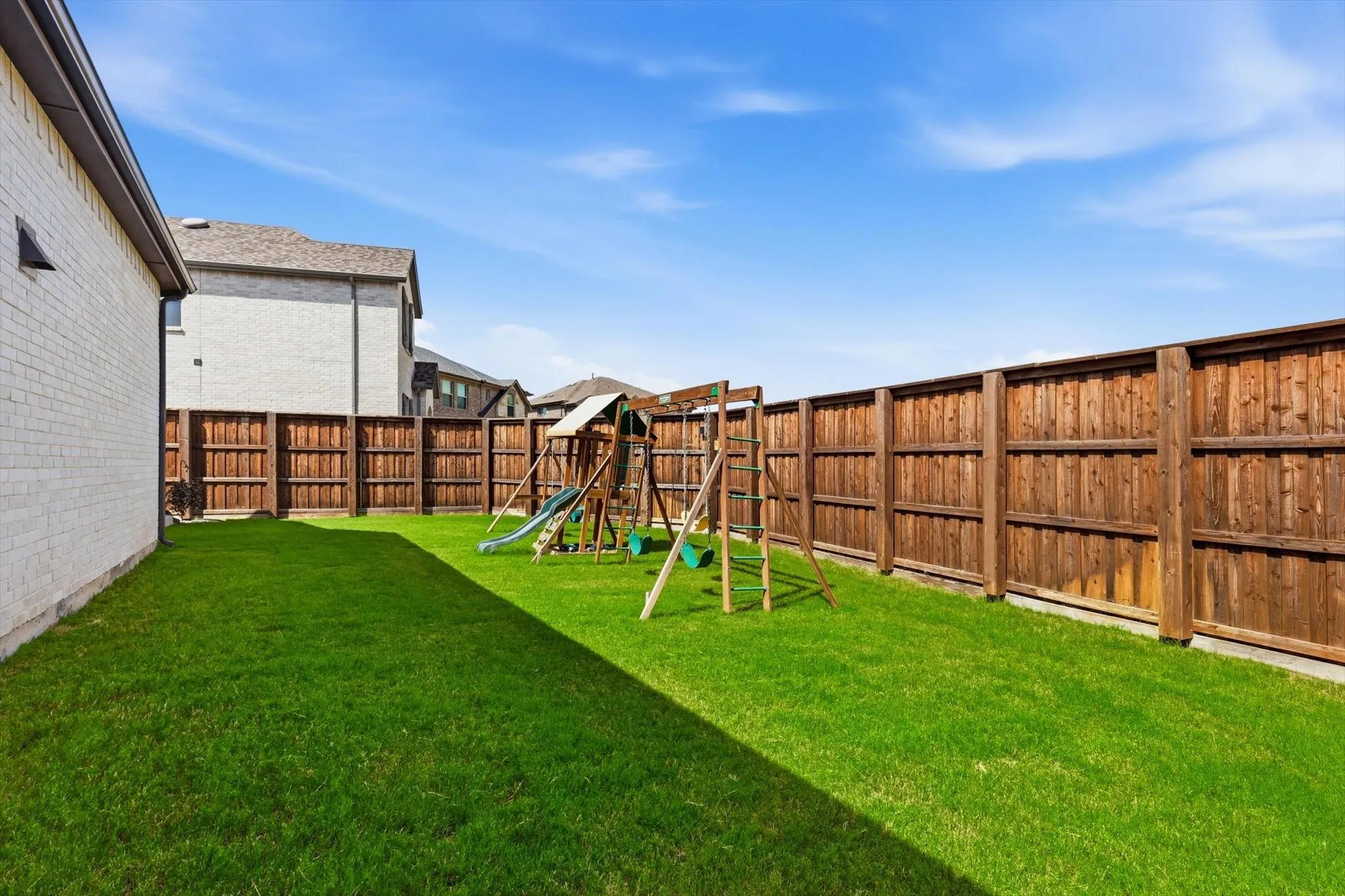 Spacious backyard featuring a manicured lawn, full wood privacy fencing, and a light-colored brick exterior