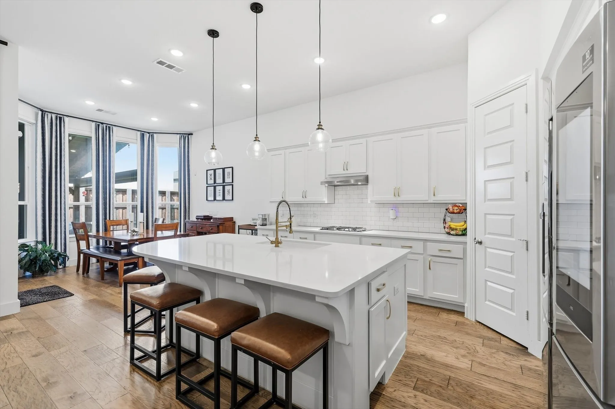 Modern kitchen featuring a large central island with seating, white shaker cabinetry, stainless steel appliances, and a subway tile backsplash
