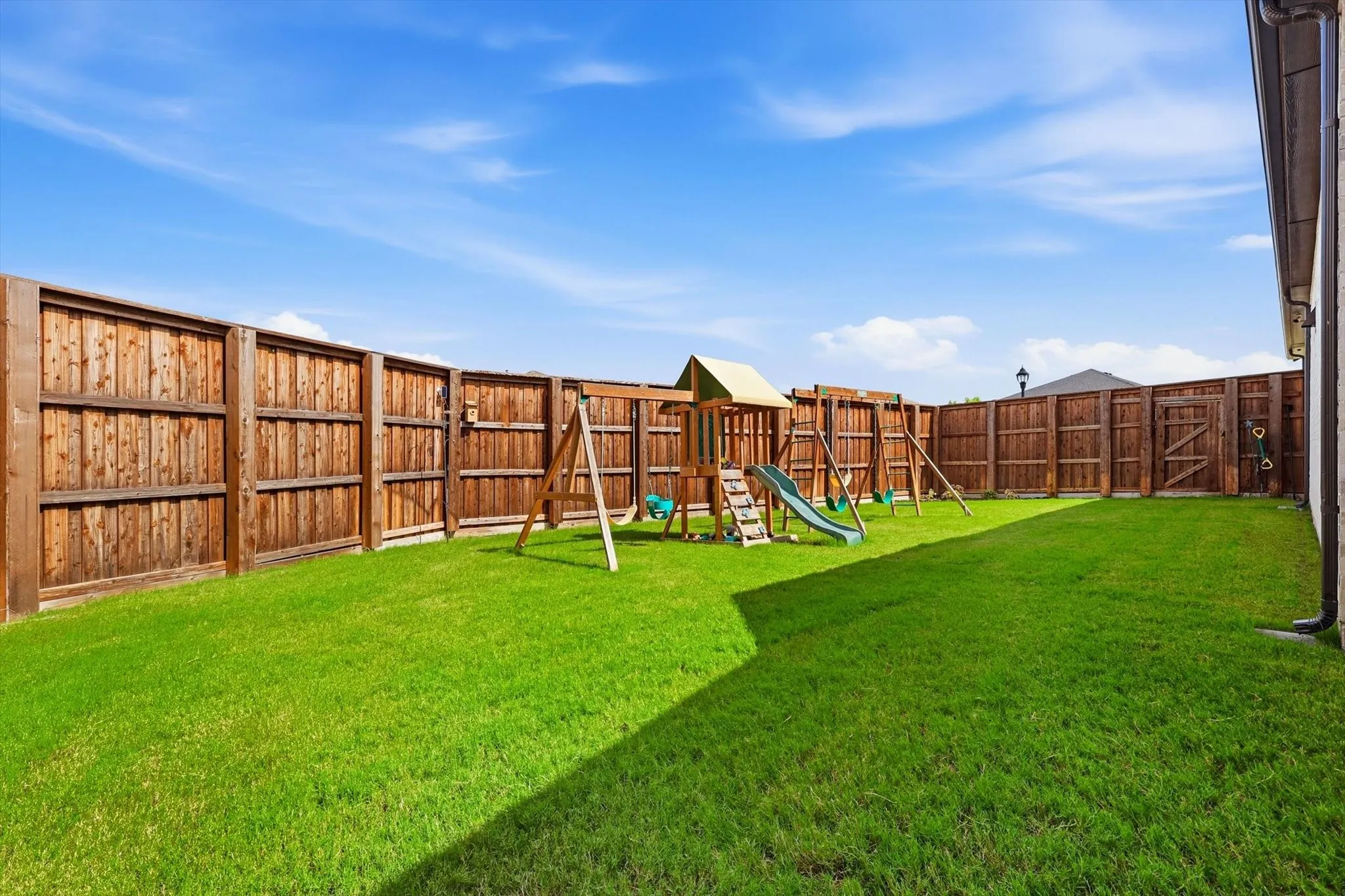 Expansive backyard featuring a wood privacy fence, substantial green lawn, and a multi-component play structure