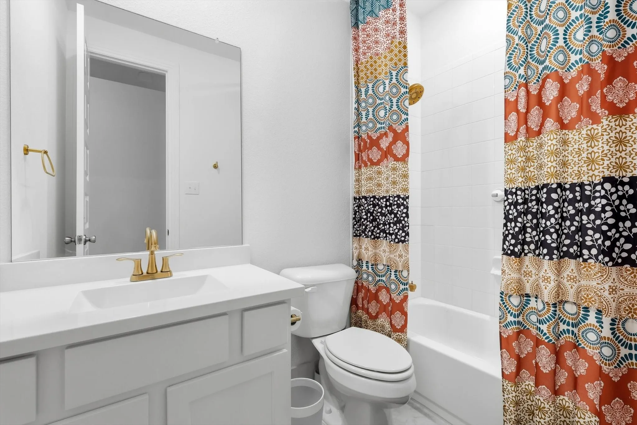 Bathroom featuring a vanity with a white countertop and integrated sink, gold-toned faucet and hardware, and a white tiled shower-over-tub combination