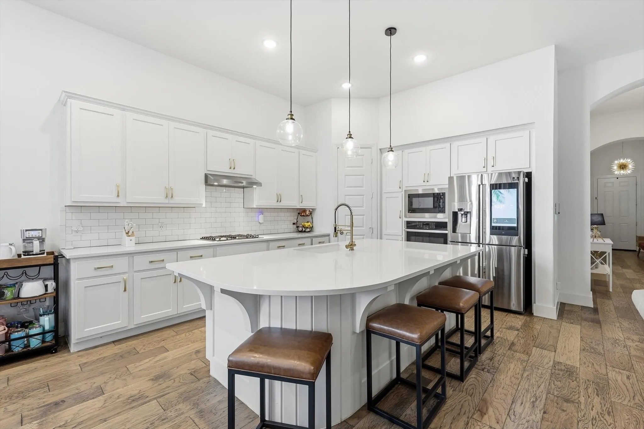 Spacious kitchen featuring an expansive central island with seating, recessed lighting, wood-finish flooring, white cabinetry, and stainless steel appliances