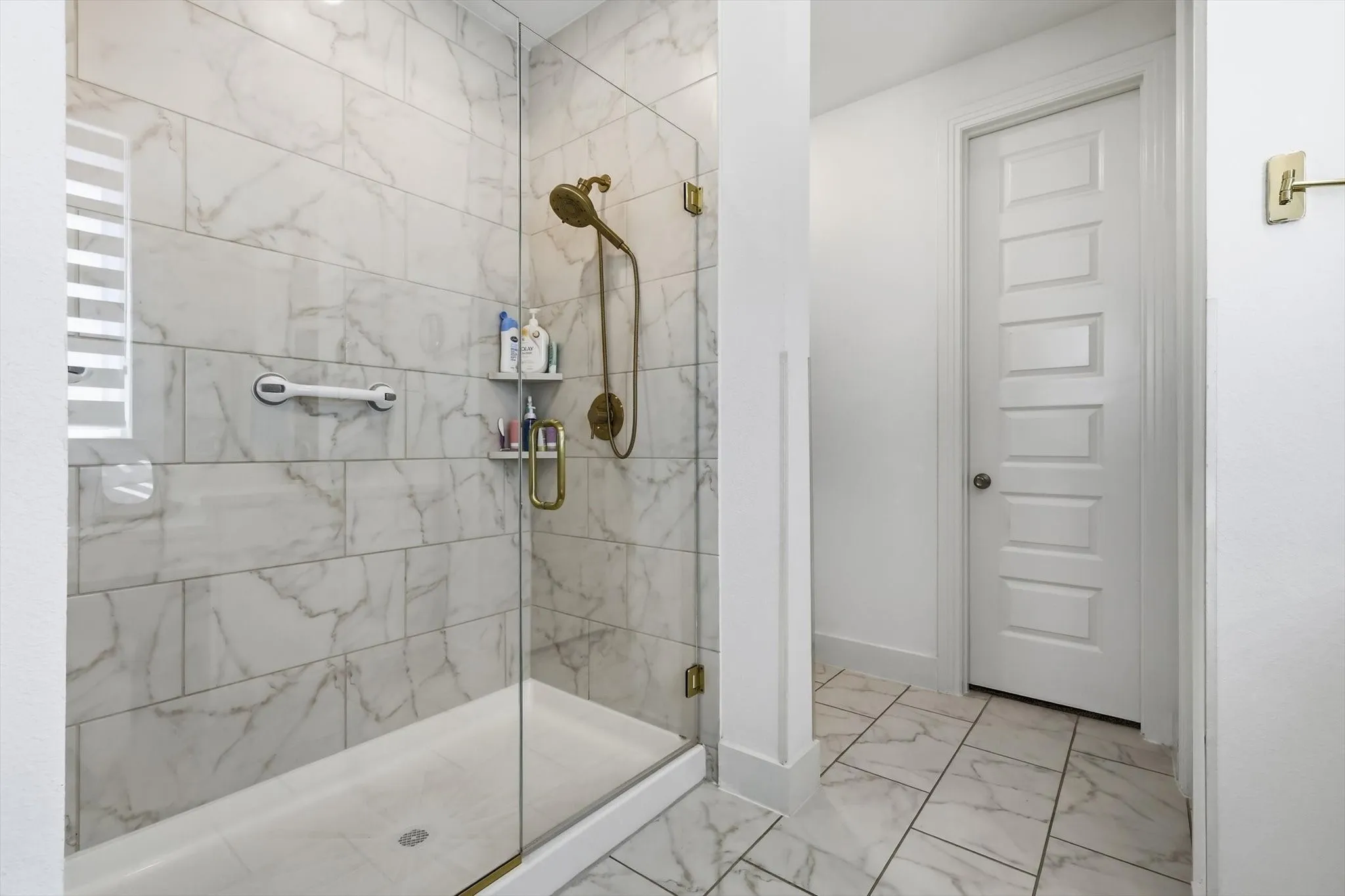 Glass-enclosed shower with full-height marble-look tile surround, a brass-finish shower system, and a built-in shower niche