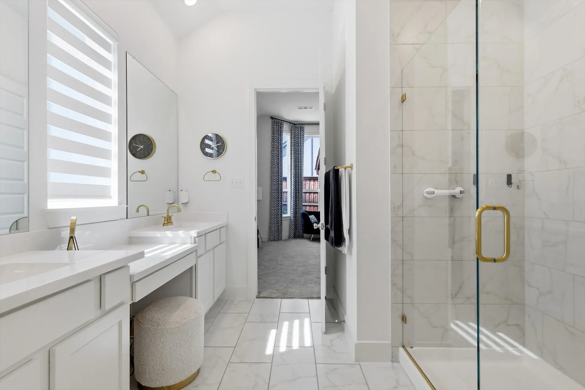 Bathroom featuring a frameless glass shower enclosure, dual vanity with undermount sinks, white cabinetry, and gold-finish fixtures