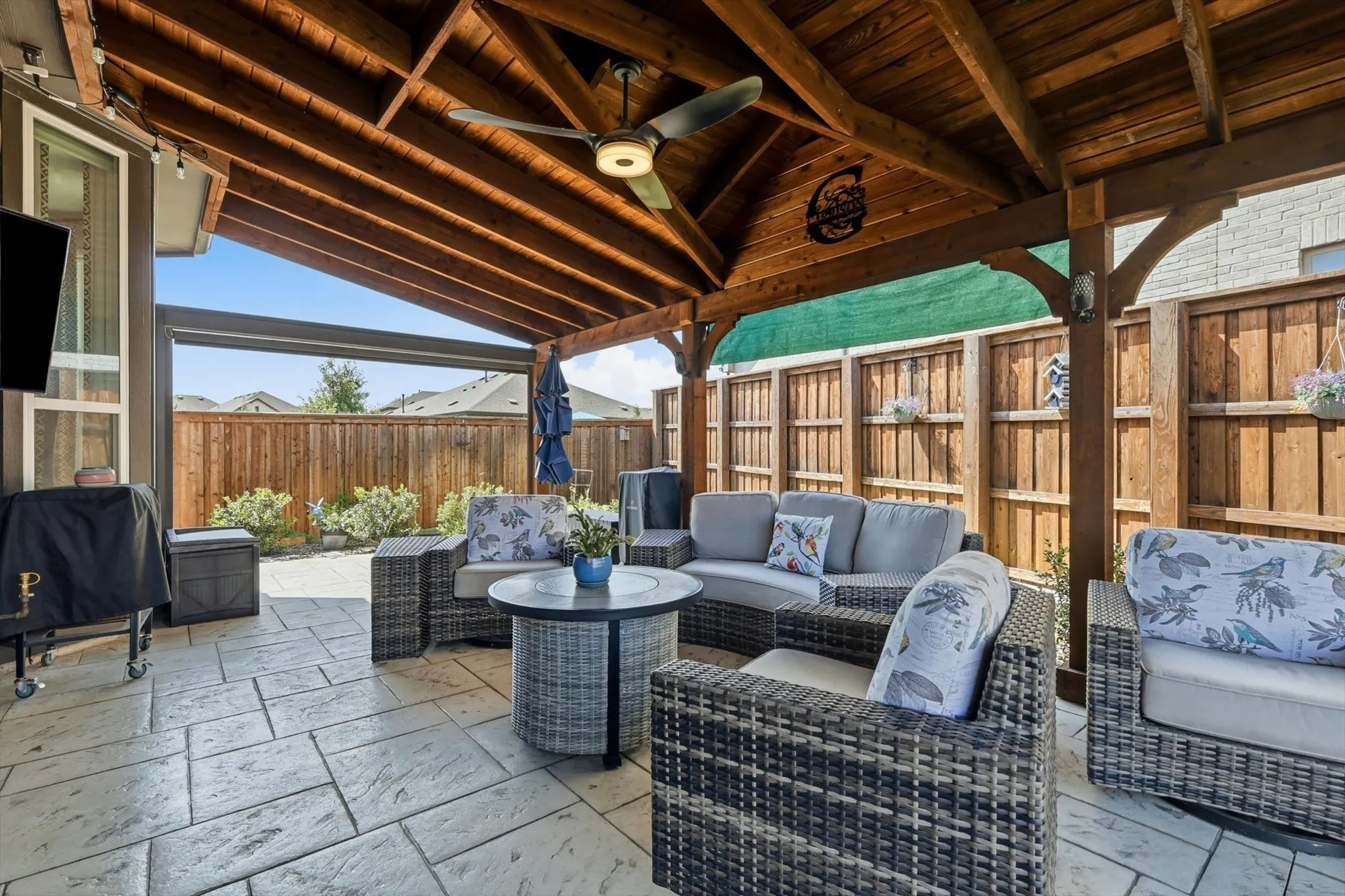 Expansive outdoor living area featuring a vaulted wood-beam ceiling, ceiling fan, and large format stamped concrete patio