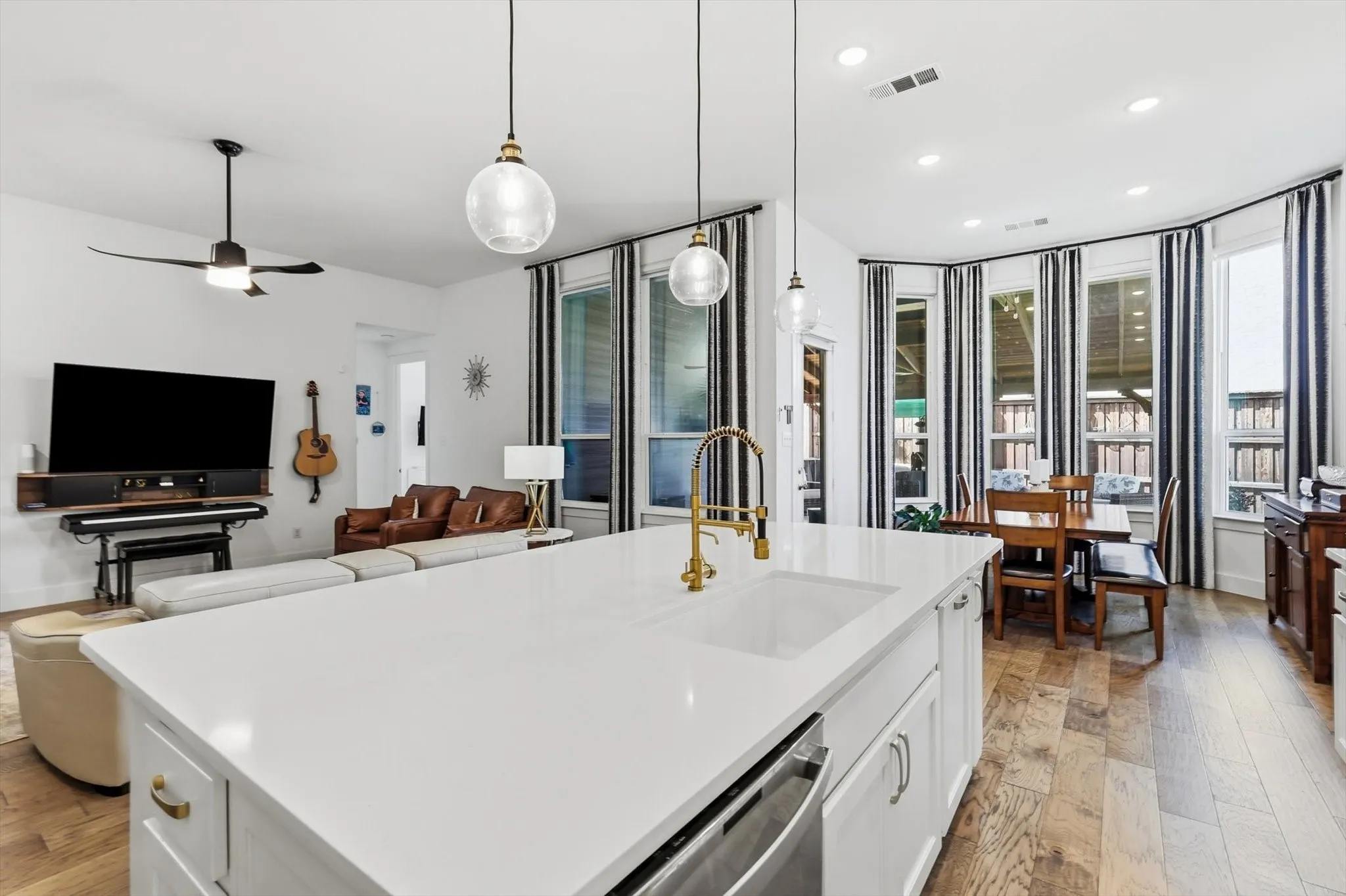 Kitchen island featuring a single-basin sink with a brass-finish faucet, under-counter dishwasher, white cabinetry, and a light-toned countertop